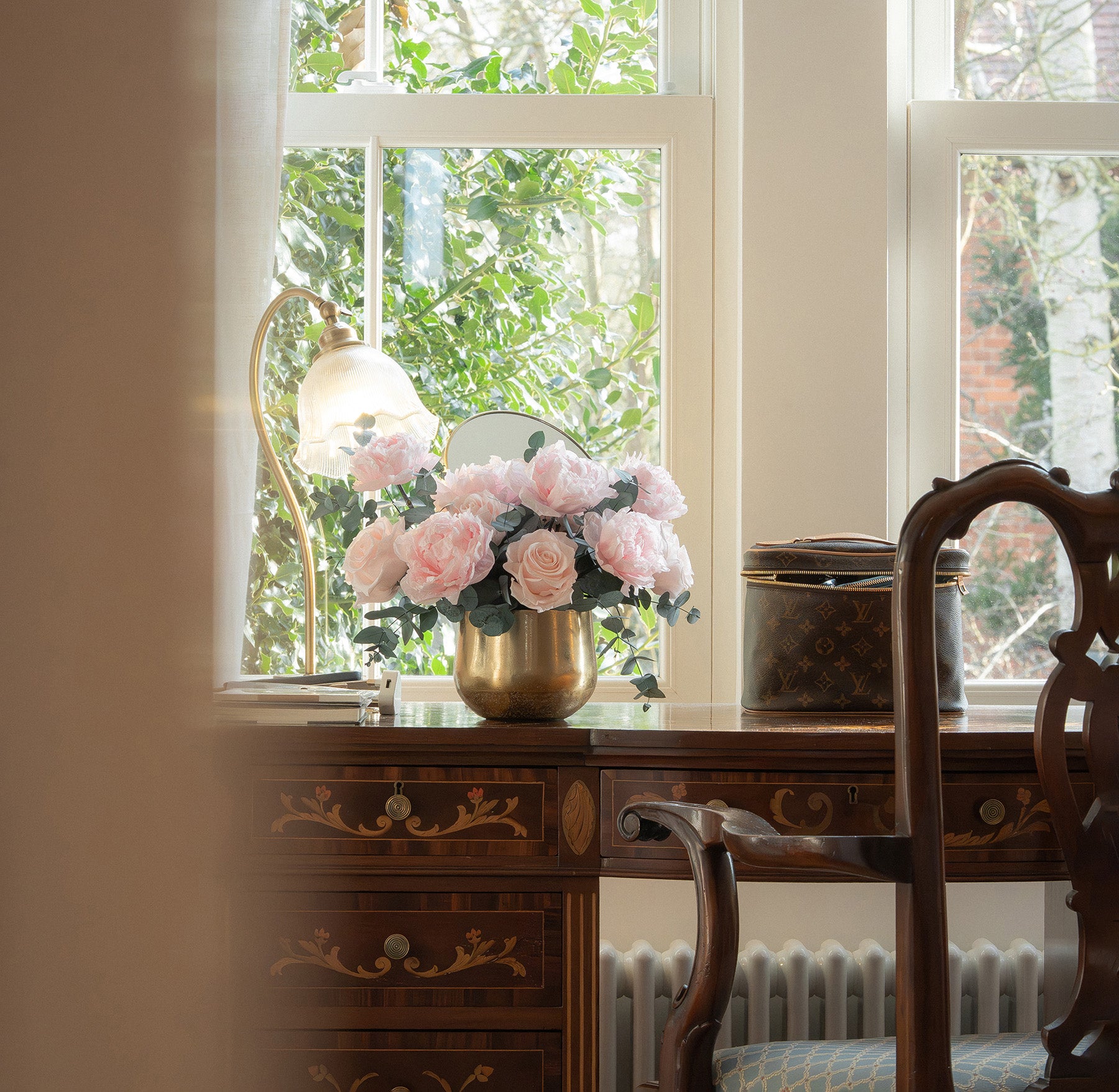 Preserved peony and rose arrangement in gold vase on a writing desk