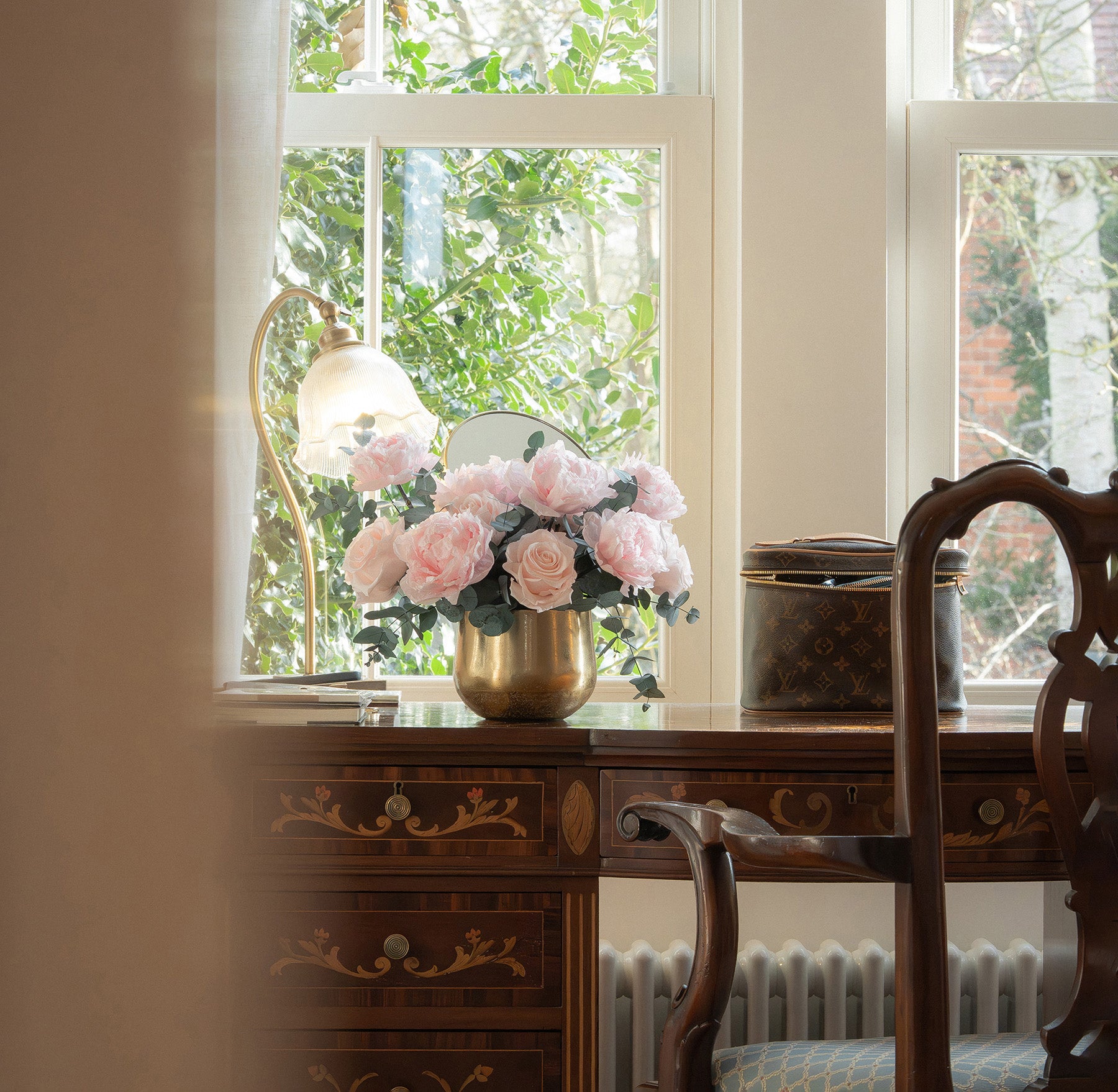 Preserved peony and rose arrangement in gold vase on a writing desk