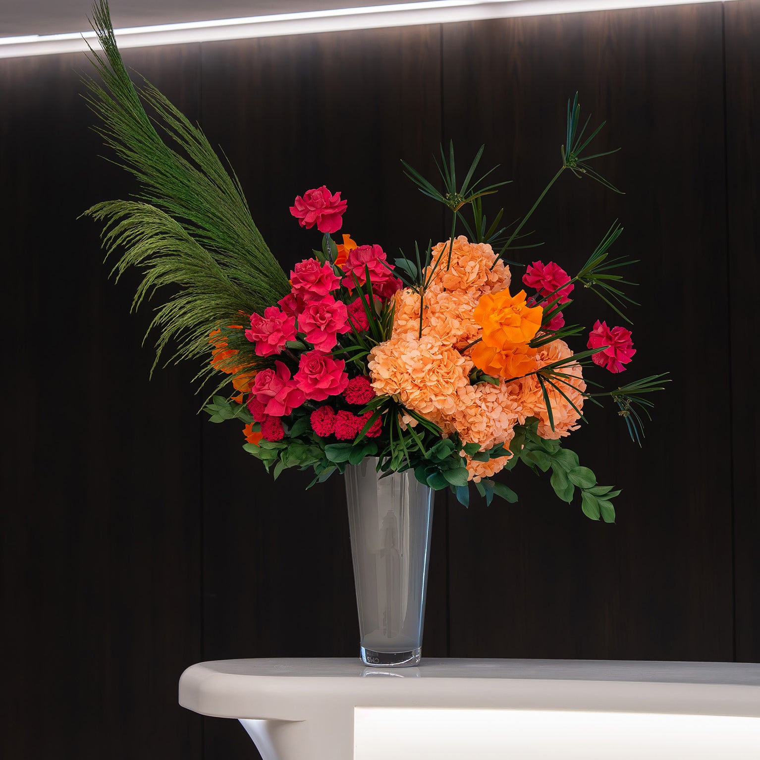 Colourful preserved flower arrangement with preserved reflexed roses and hydrangeas in a grey vase on office lobby table