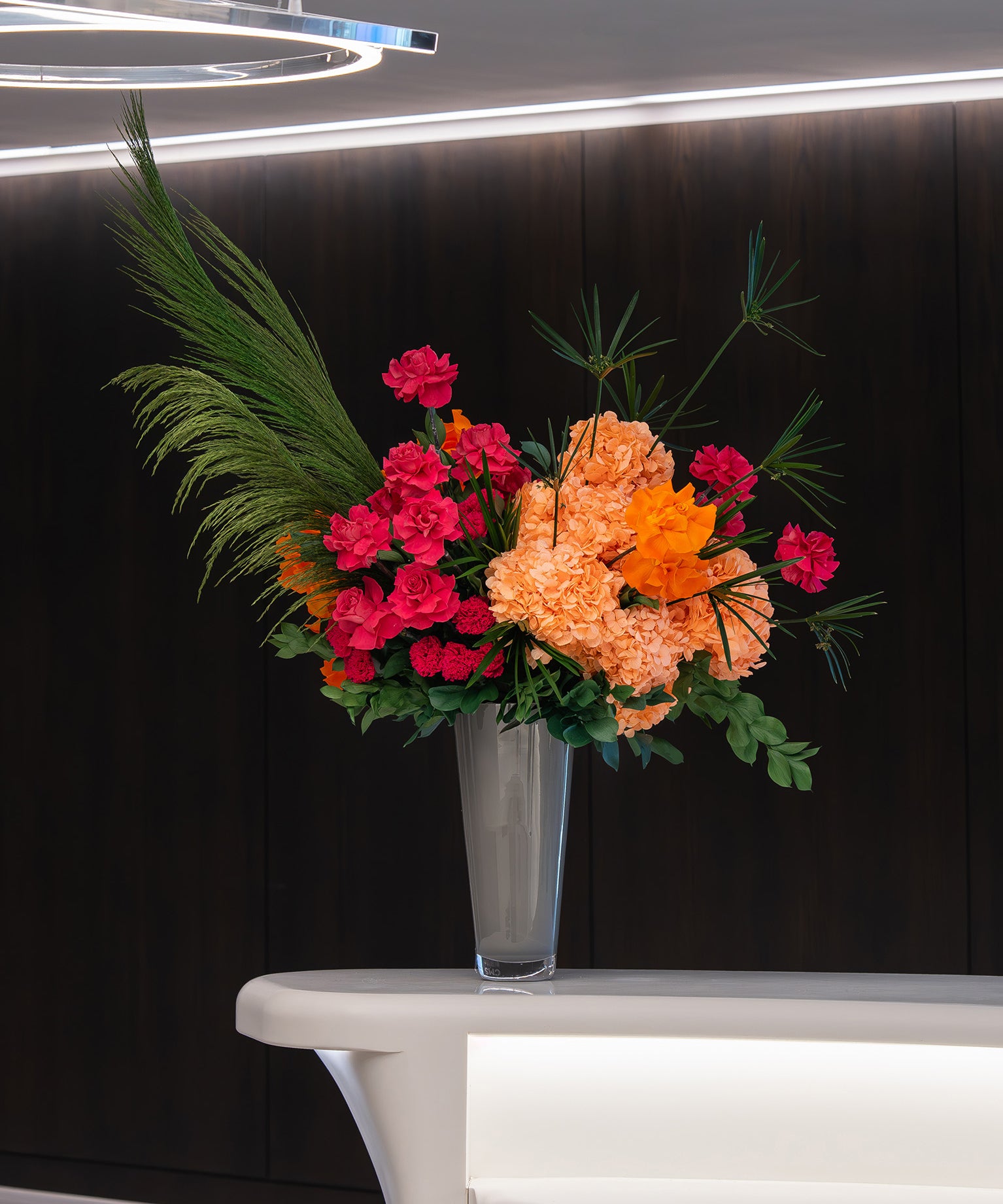 Colourful preserved flower arrangement with preserved reflexed roses and hydrangeas in a grey vase on office lobby table