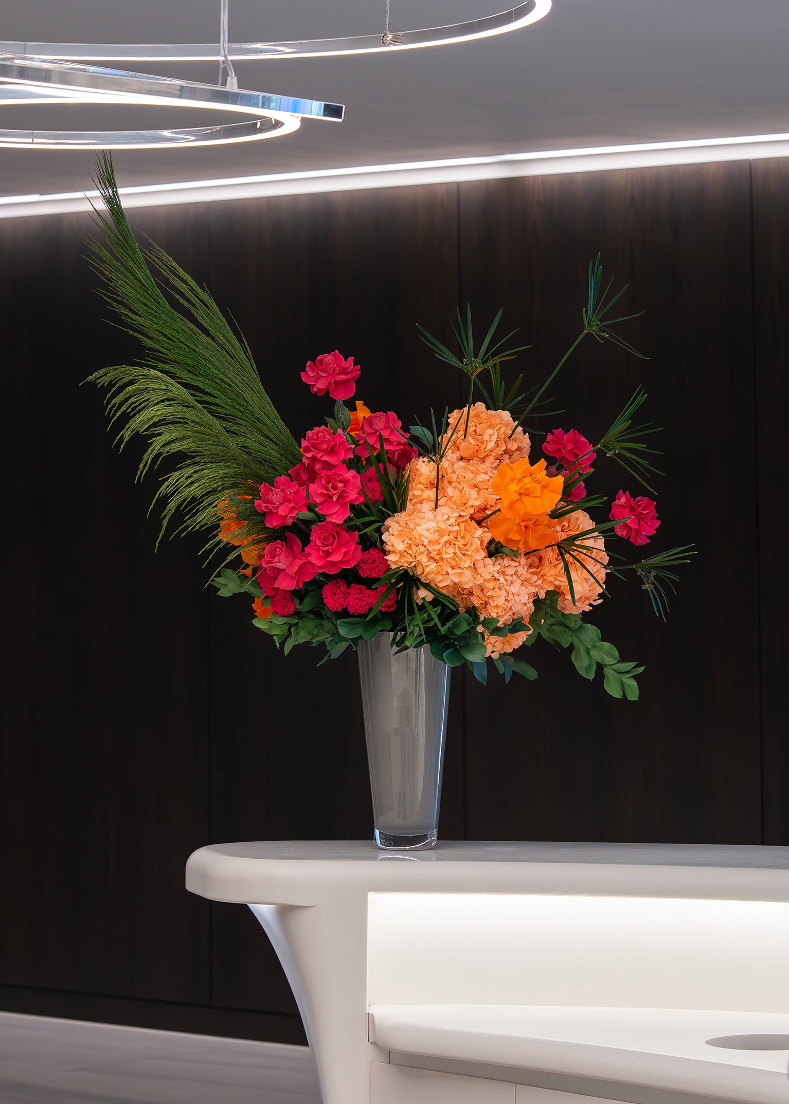 Colourful preserved flower arrangement with preserved reflexed roses and hydrangeas in a grey vase on office lobby table