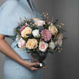 A preserved blush and peach gardenia and roses, gardenia arrangement with foliage in silver vase