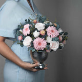 A preserved pink roses, gerbera, carnation and filler flowers arrangement with foliage in silver vase