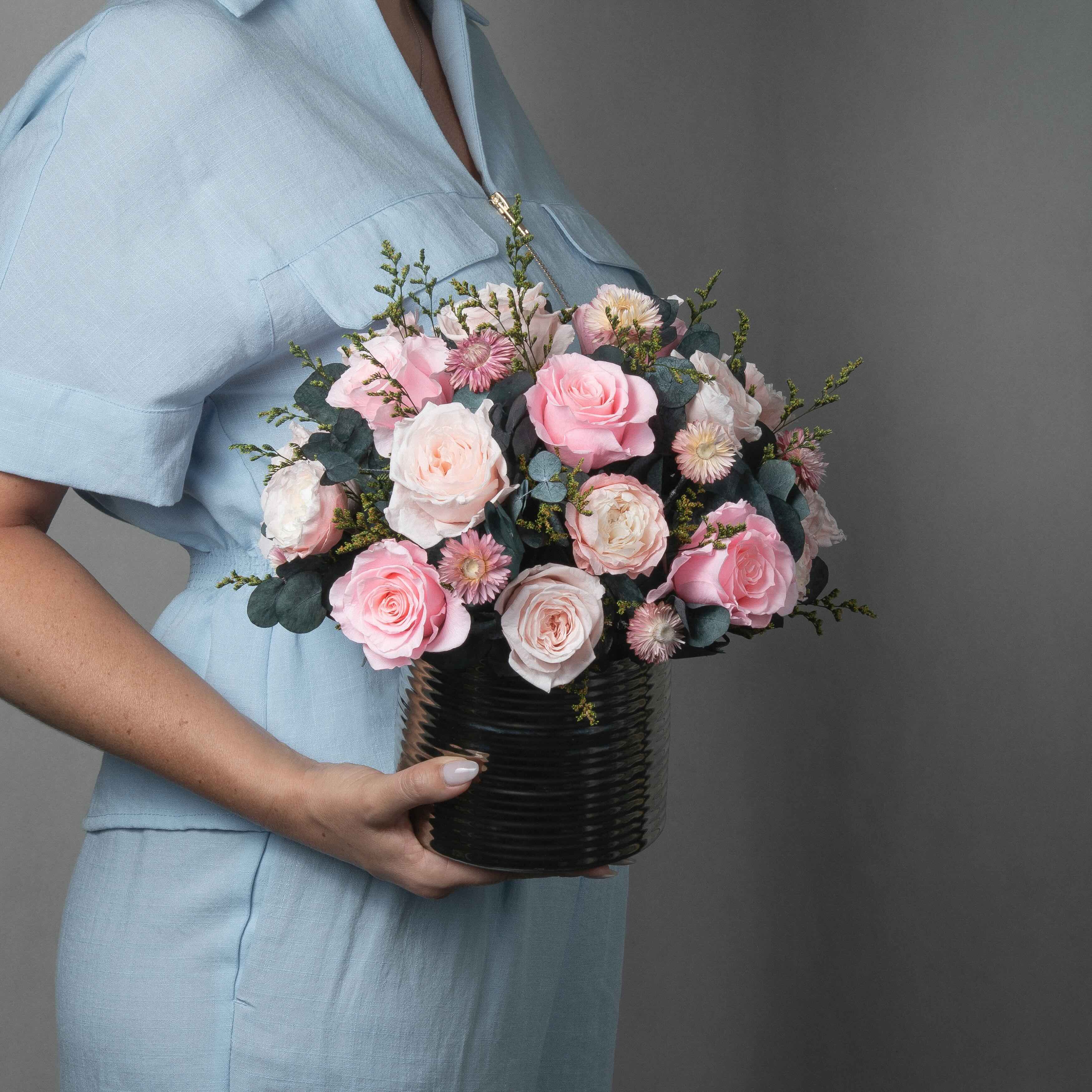 A preserved pink roses and filler flowers arrangement with foliage in silver vase