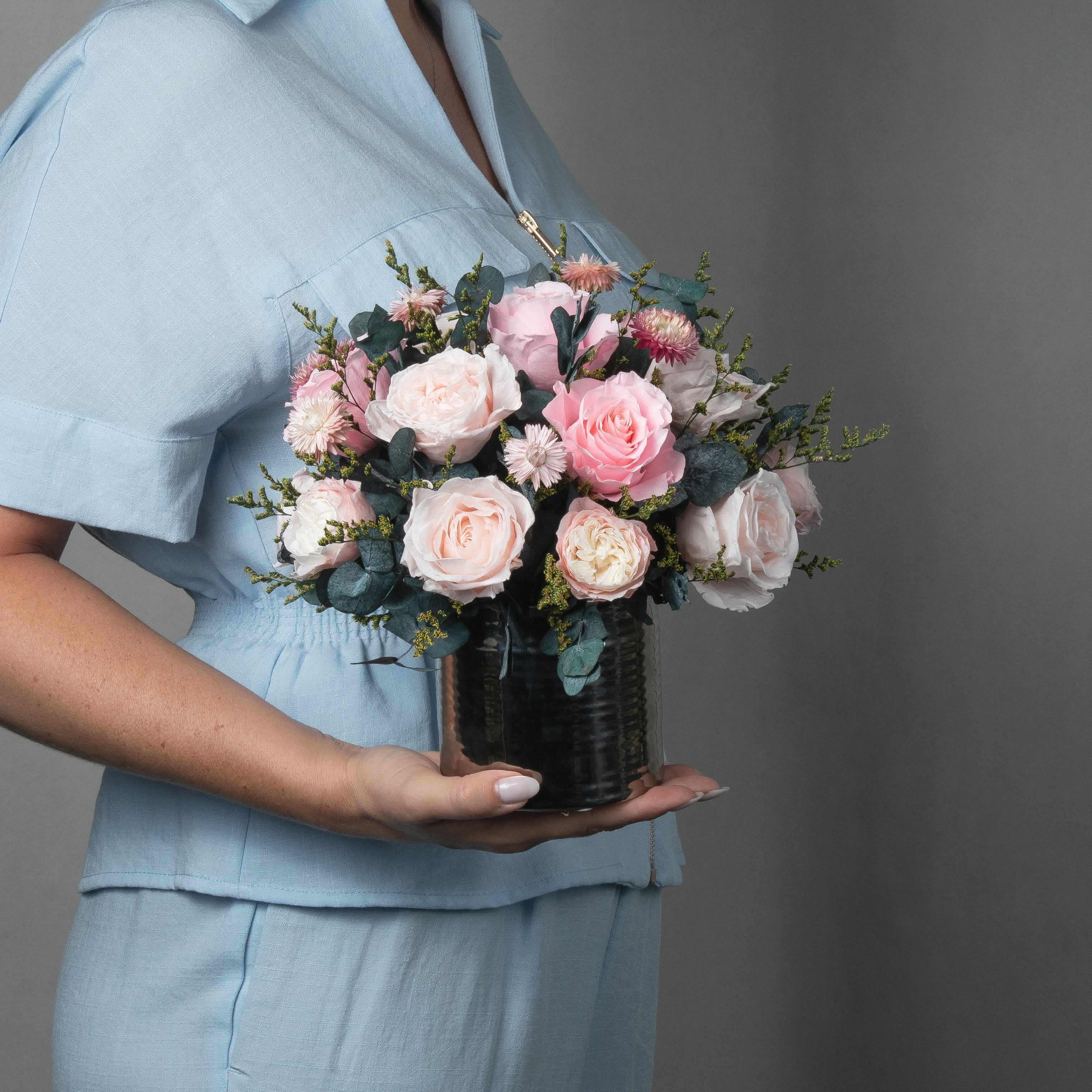 A preserved pink roses and filler flowers arrangement with foliage in silver vase