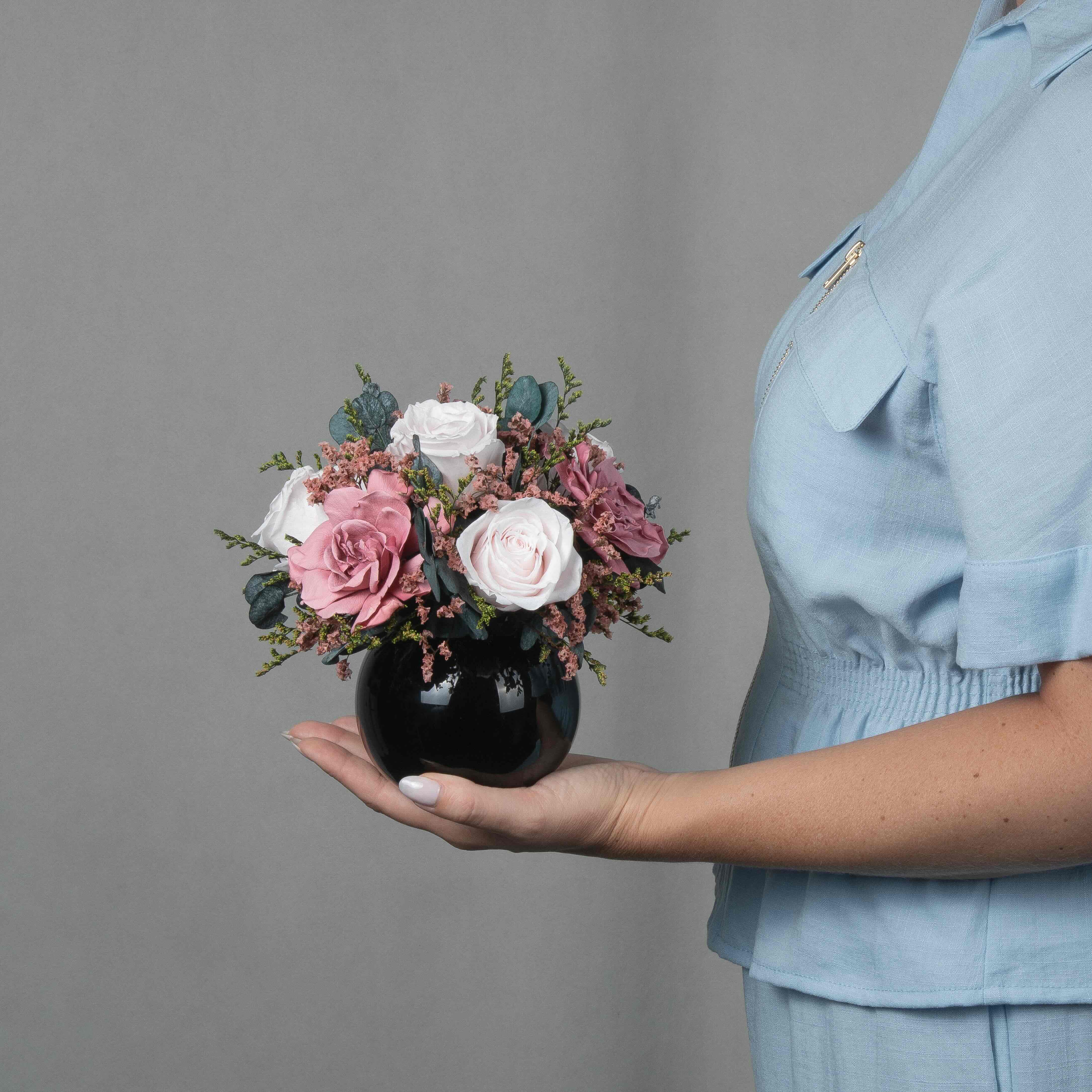 A preserved rose and gardenia arrangement with preserved foliage in black round vase