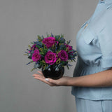 A preserved magenta rose arrangement with preserved foliage in black round vase