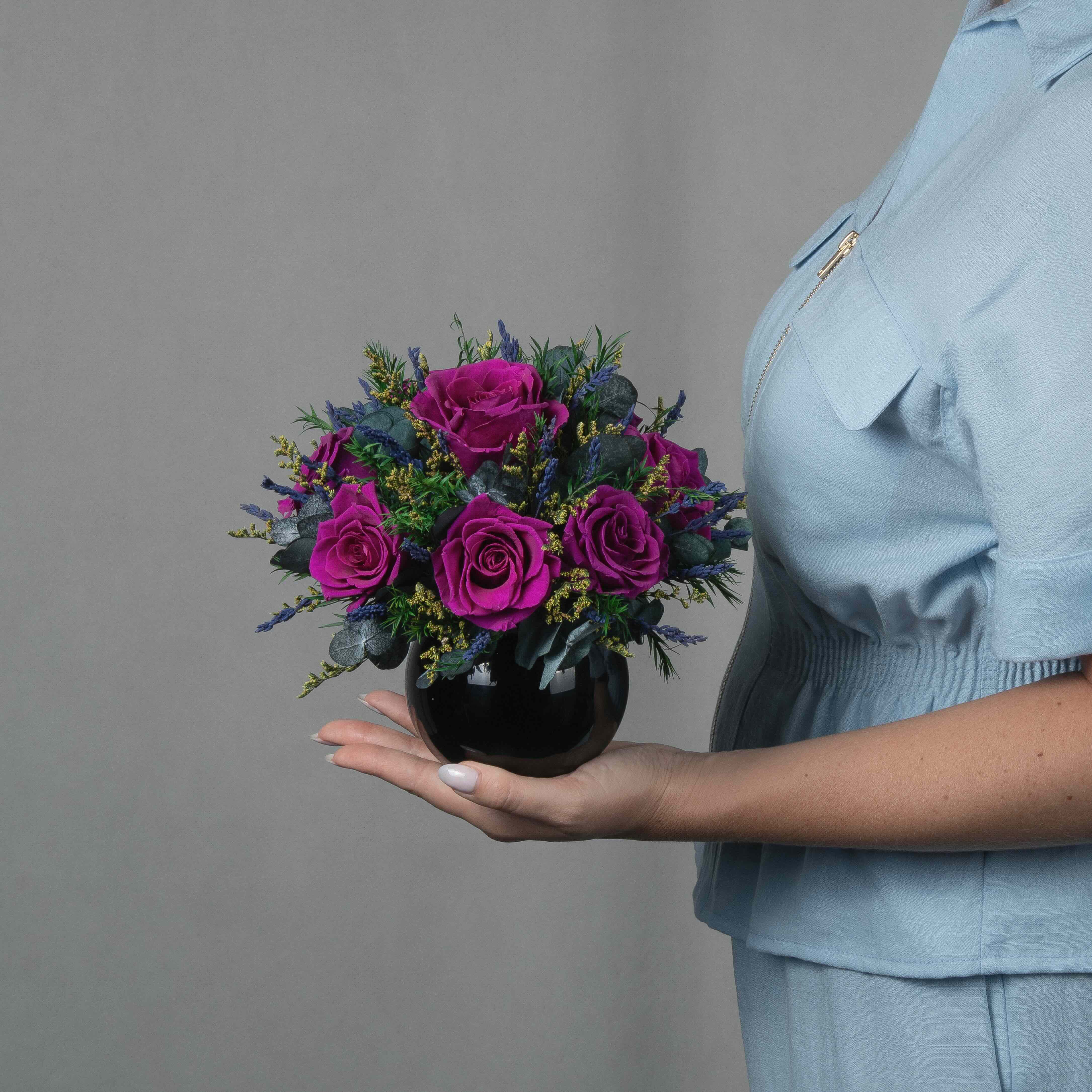 A preserved magenta rose arrangement with preserved foliage in black round vase