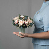 A preserved peach and pink rose arrangement in green vase