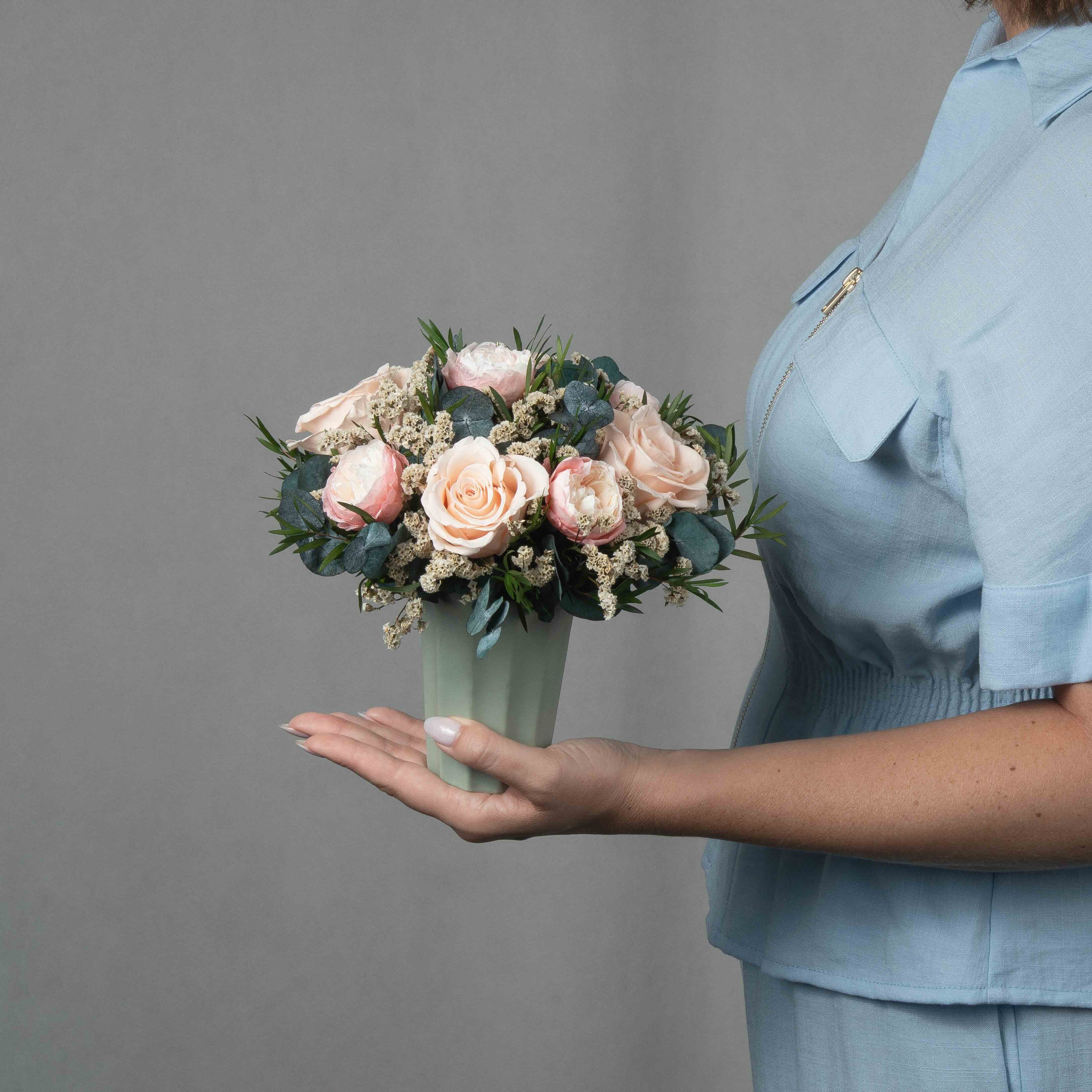 A preserved peach and pink rose arrangement in green vase