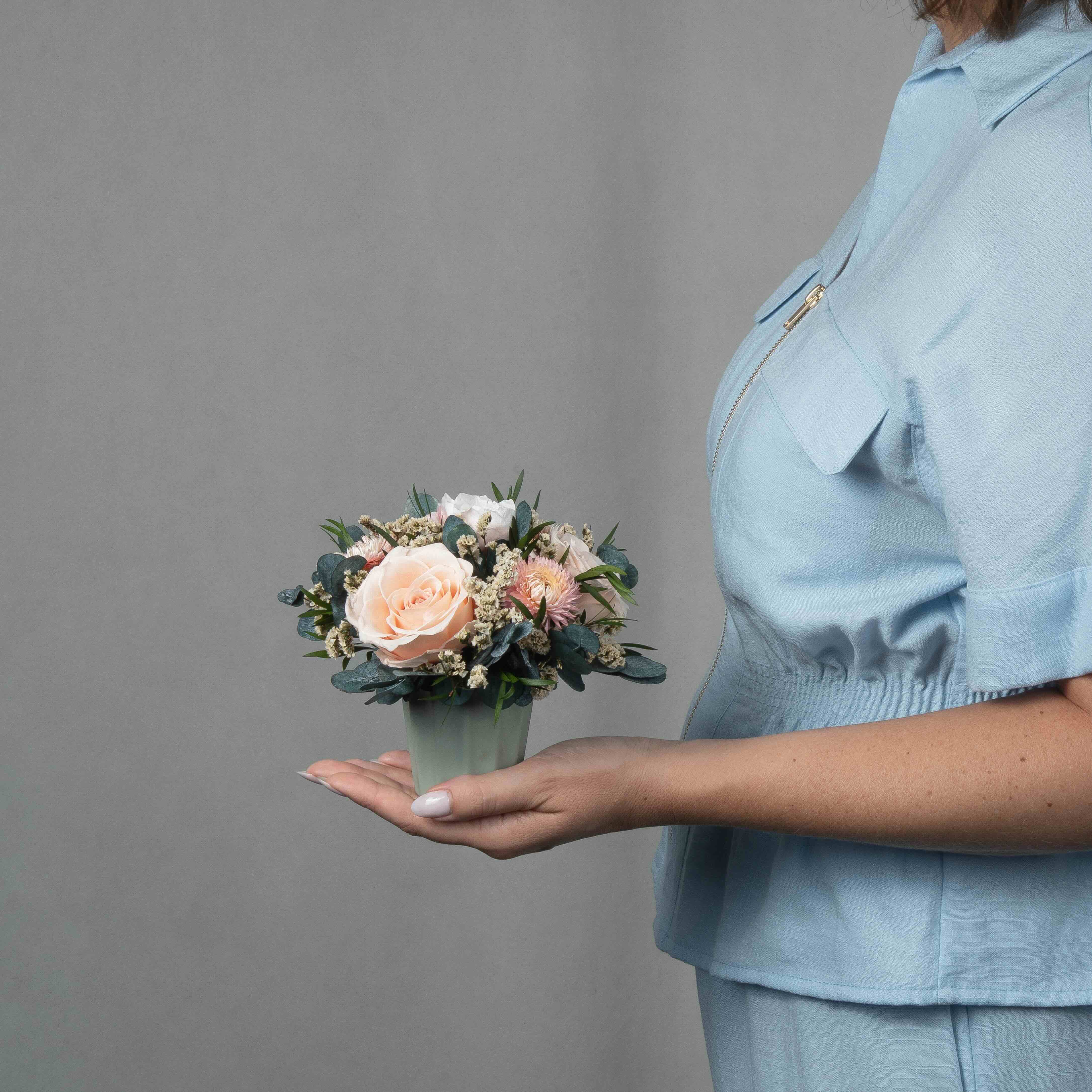 A preserved peach and pink rose arrangement with preserved foliage in green vase