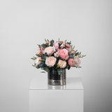A preserved pink roses and filler flowers arrangement with foliage in silver vase