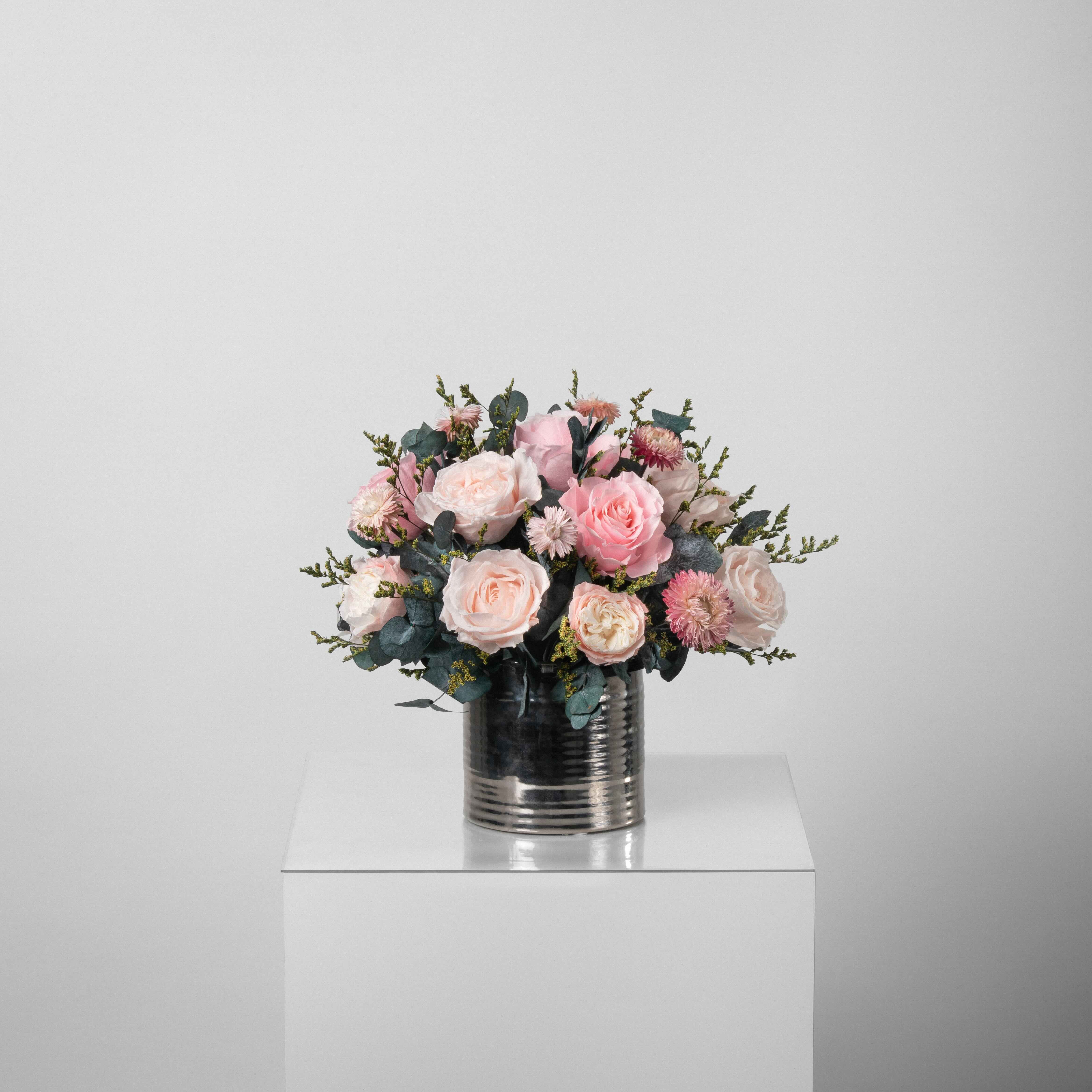 A preserved pink roses and filler flowers arrangement with foliage in silver vase