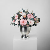 A preserved pink roses, gerbera, carnation and filler flowers arrangement with foliage in silver vase