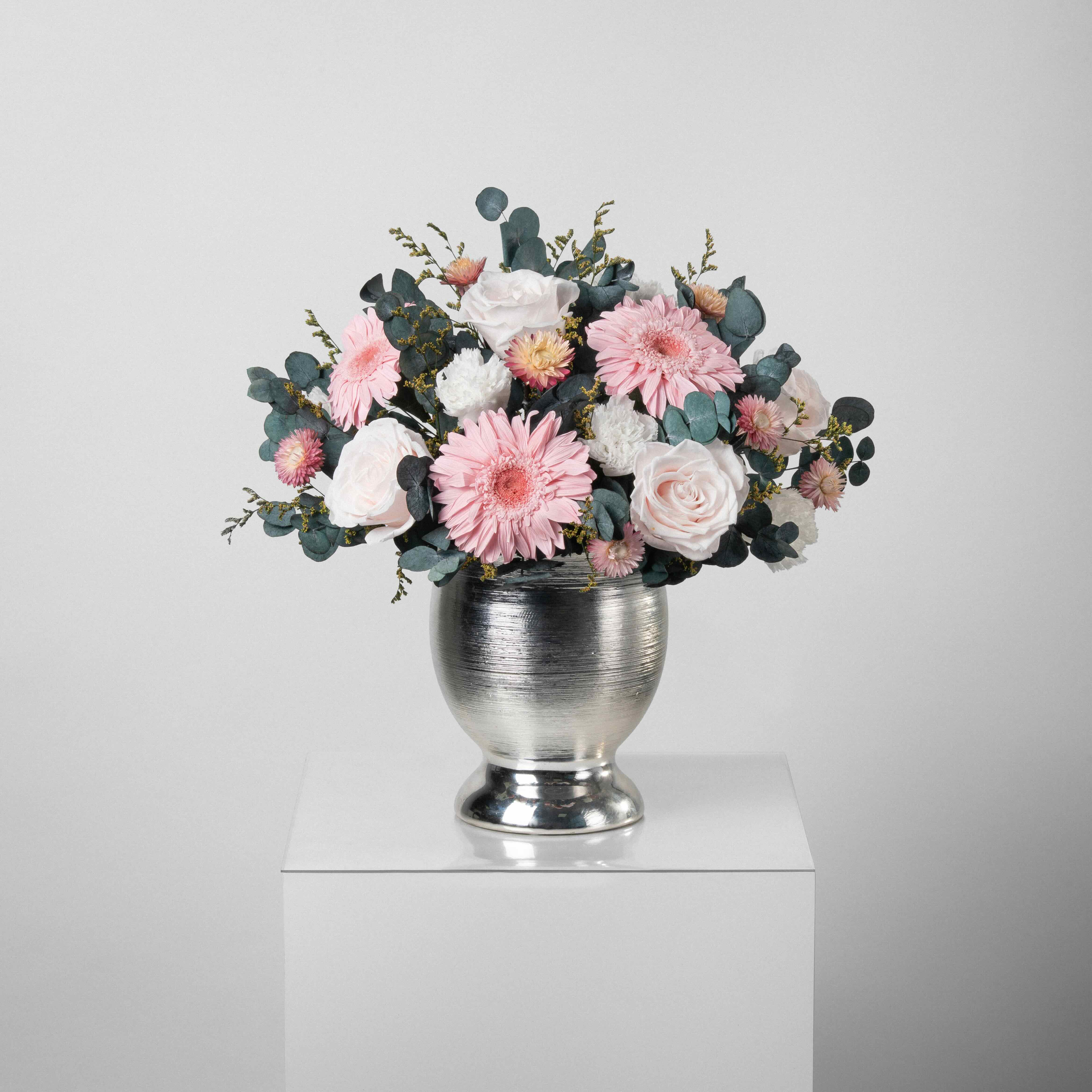 A preserved pink roses, gerbera, carnation and filler flowers arrangement with foliage in silver vase