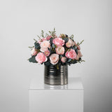 A preserved pink roses and filler flowers arrangement with foliage in silver vase
