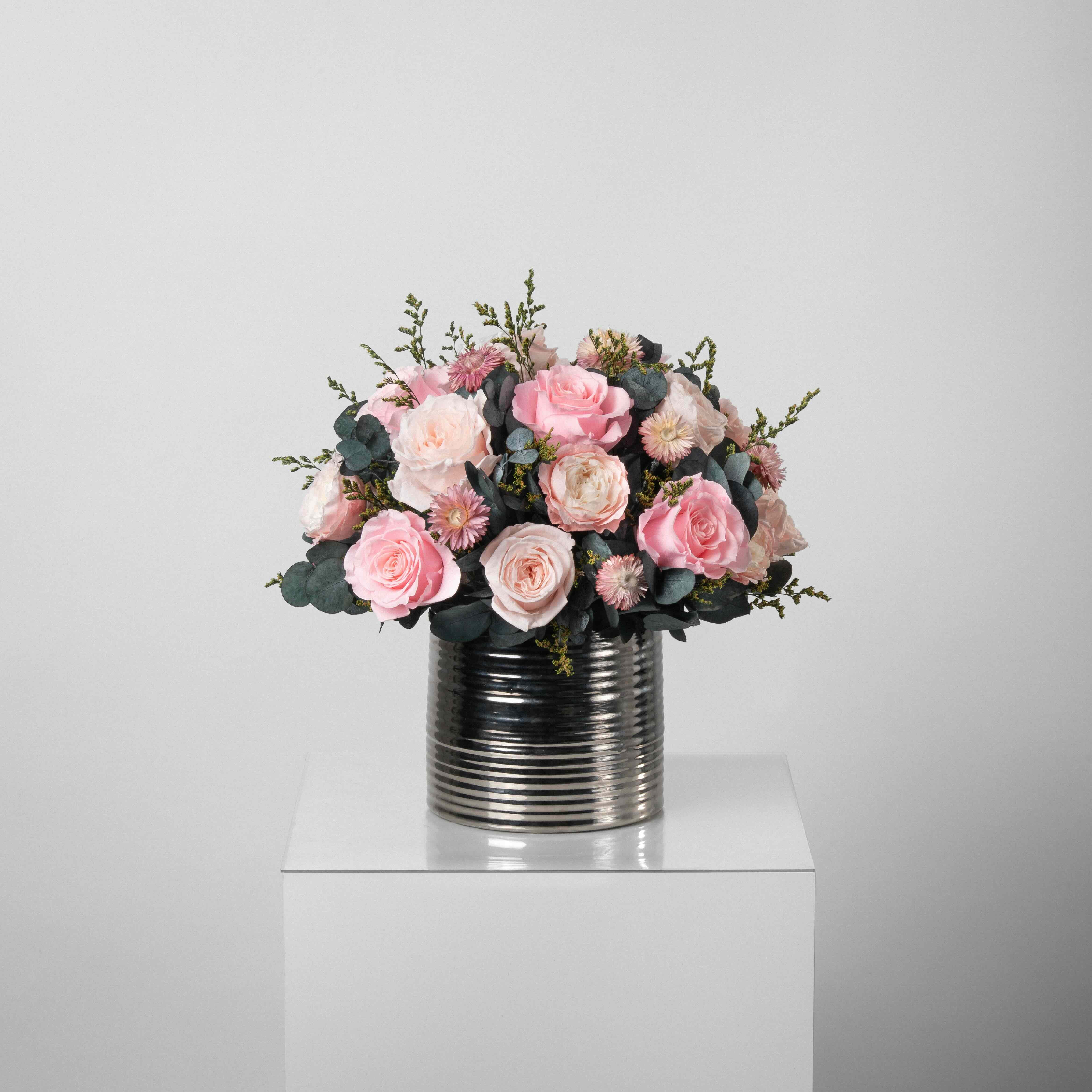 A preserved pink roses and filler flowers arrangement with foliage in silver vase