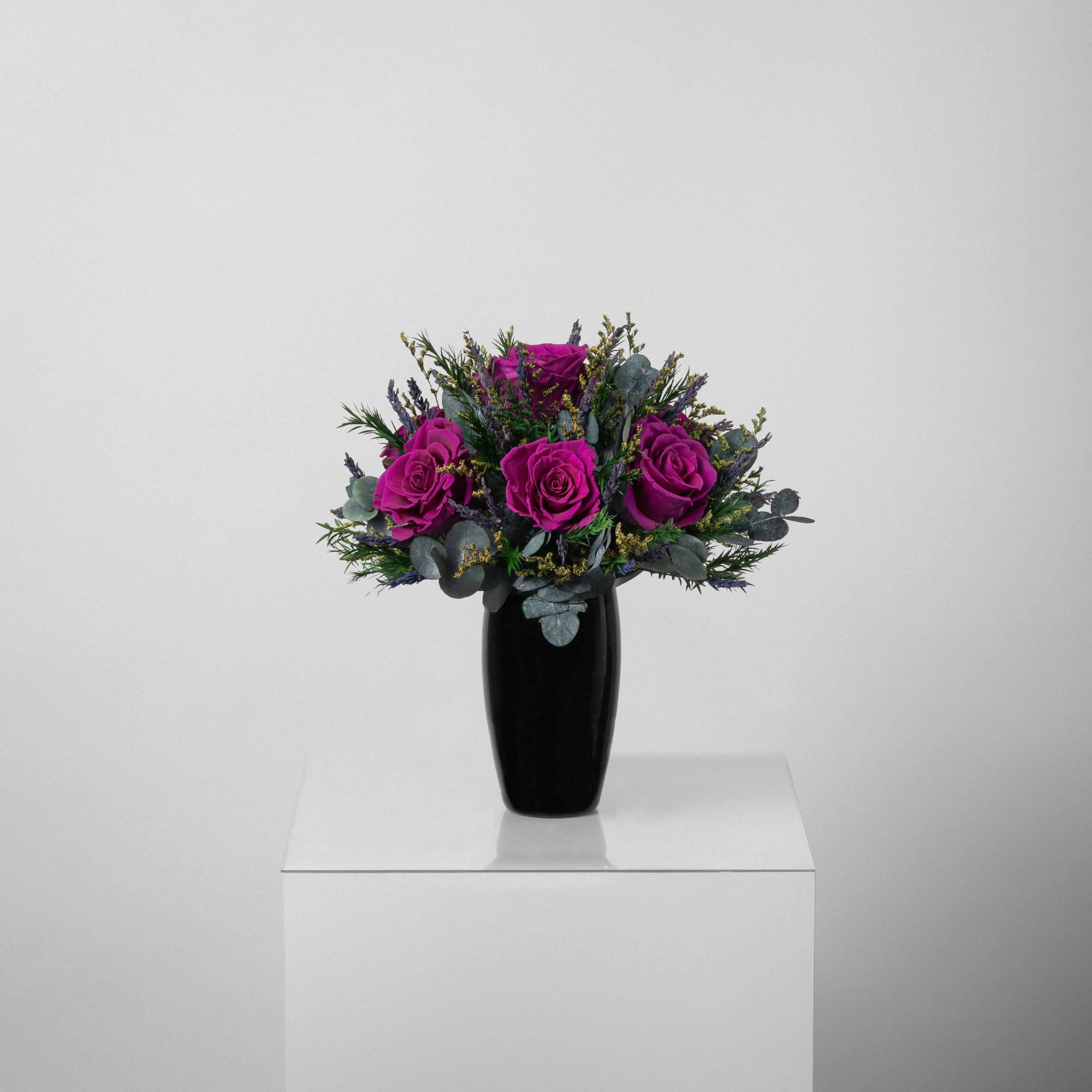 A preserved magenta rose arrangement with lavender in black vase