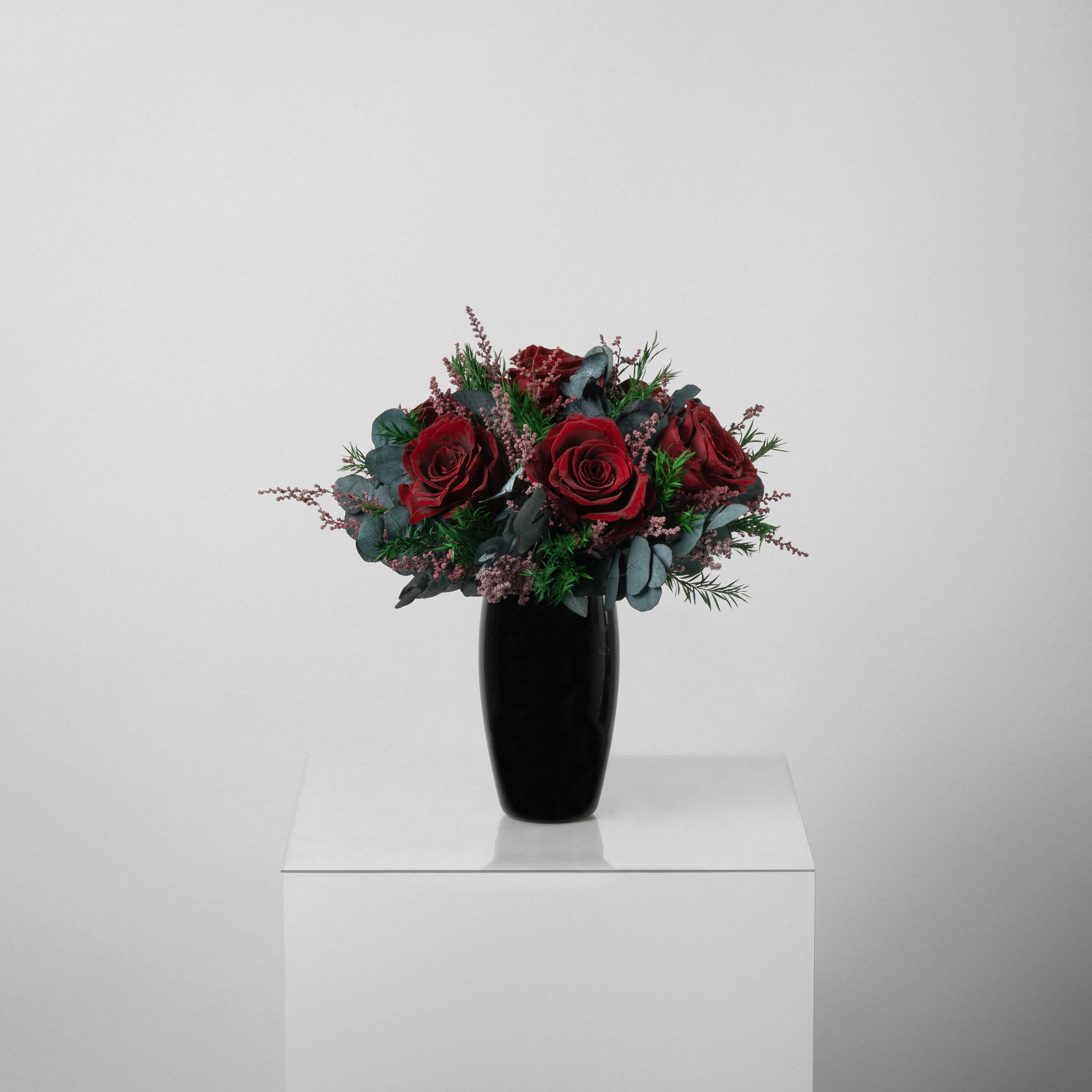 A preserved burgundy rose arrangement with lavender in black vase