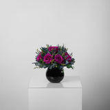 A preserved magenta rose arrangement with preserved foliage in black round vase