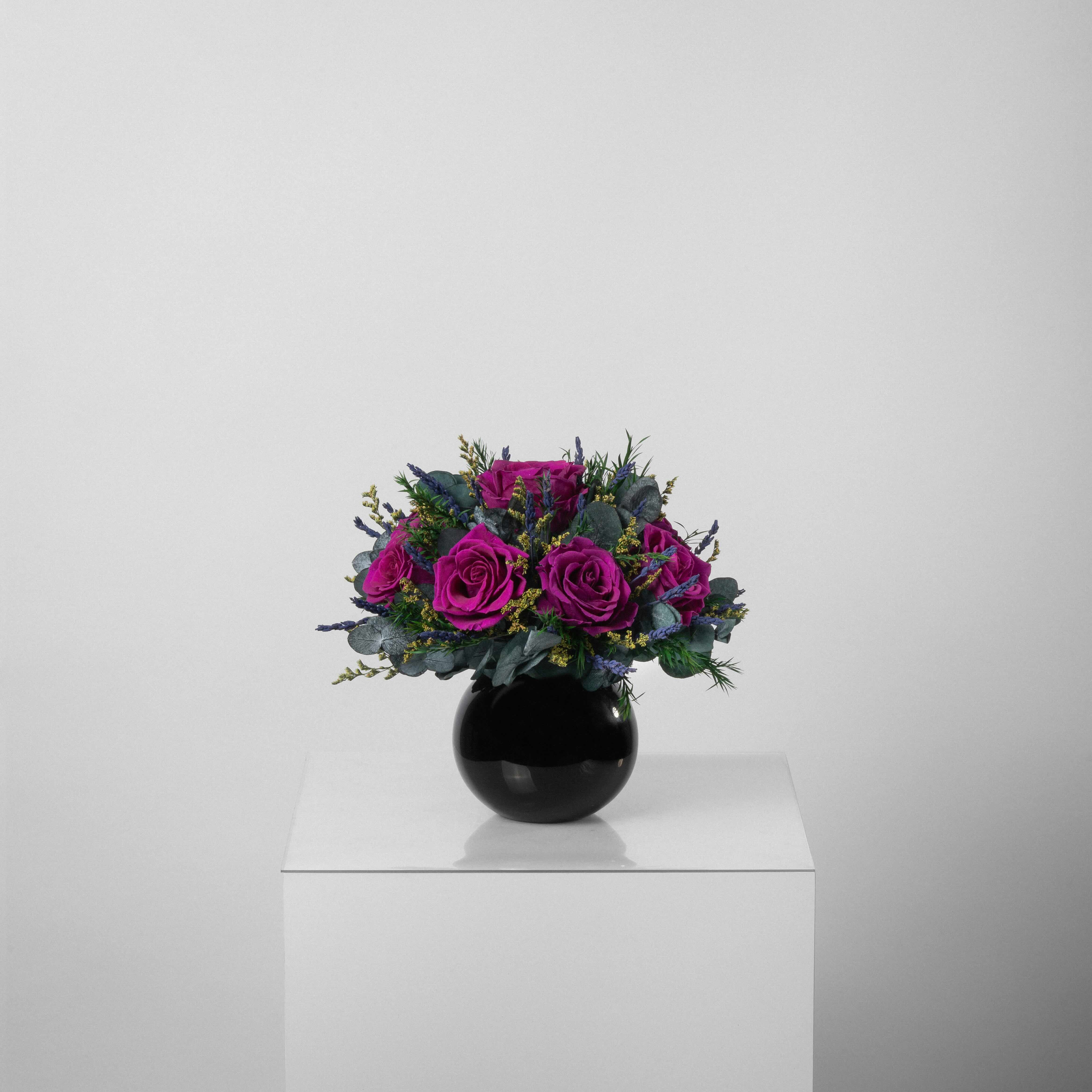 A preserved magenta rose arrangement with preserved foliage in black round vase