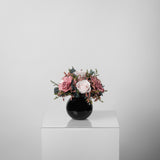 A preserved rose and gardenia arrangement with preserved foliage in black round vase