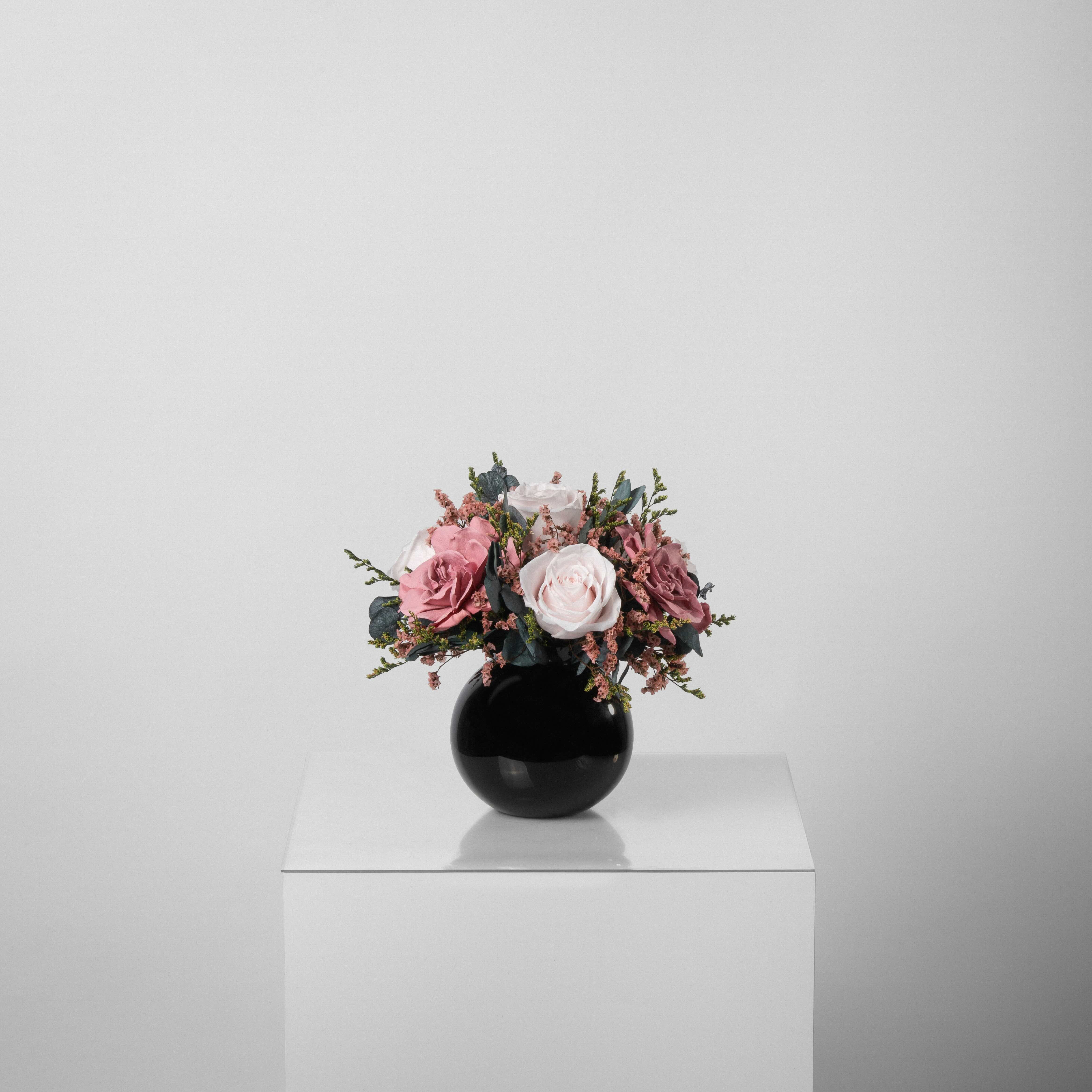 A preserved rose and gardenia arrangement with preserved foliage in black round vase