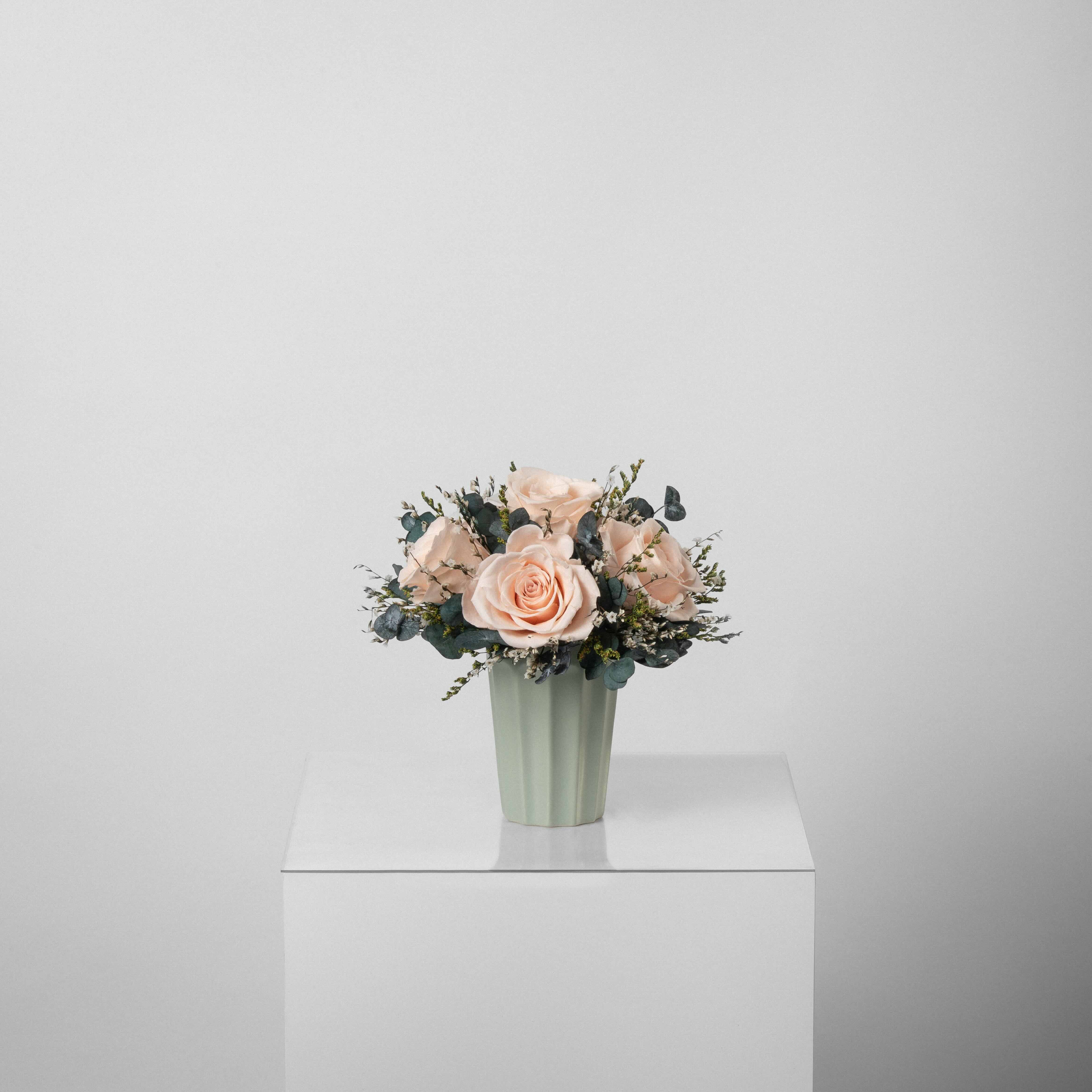 A preserved peach rose arrangement in green vase
