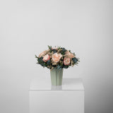 A preserved peach and pink rose arrangement in green vase