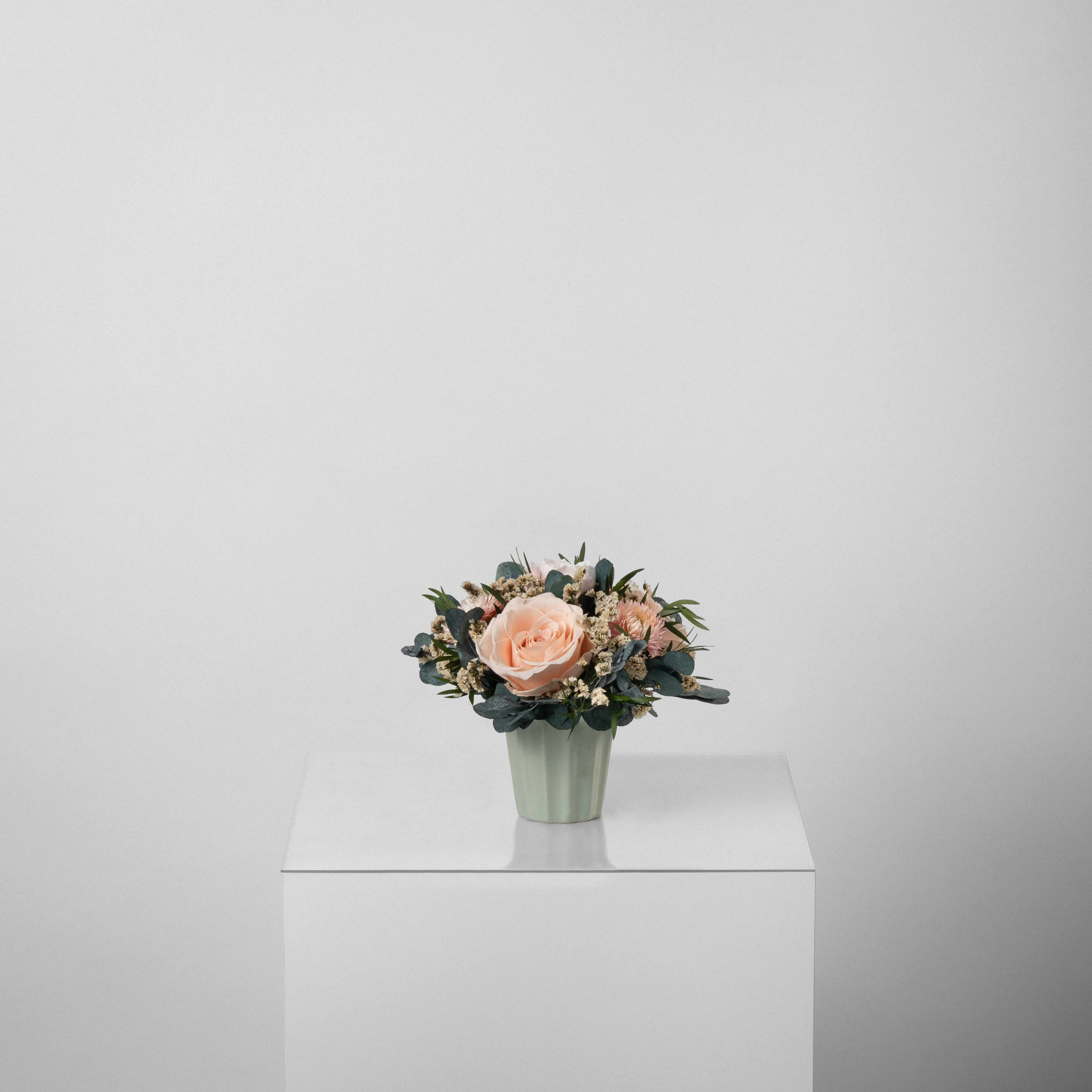 A preserved peach and pink rose arrangement with preserved foliage in green vase