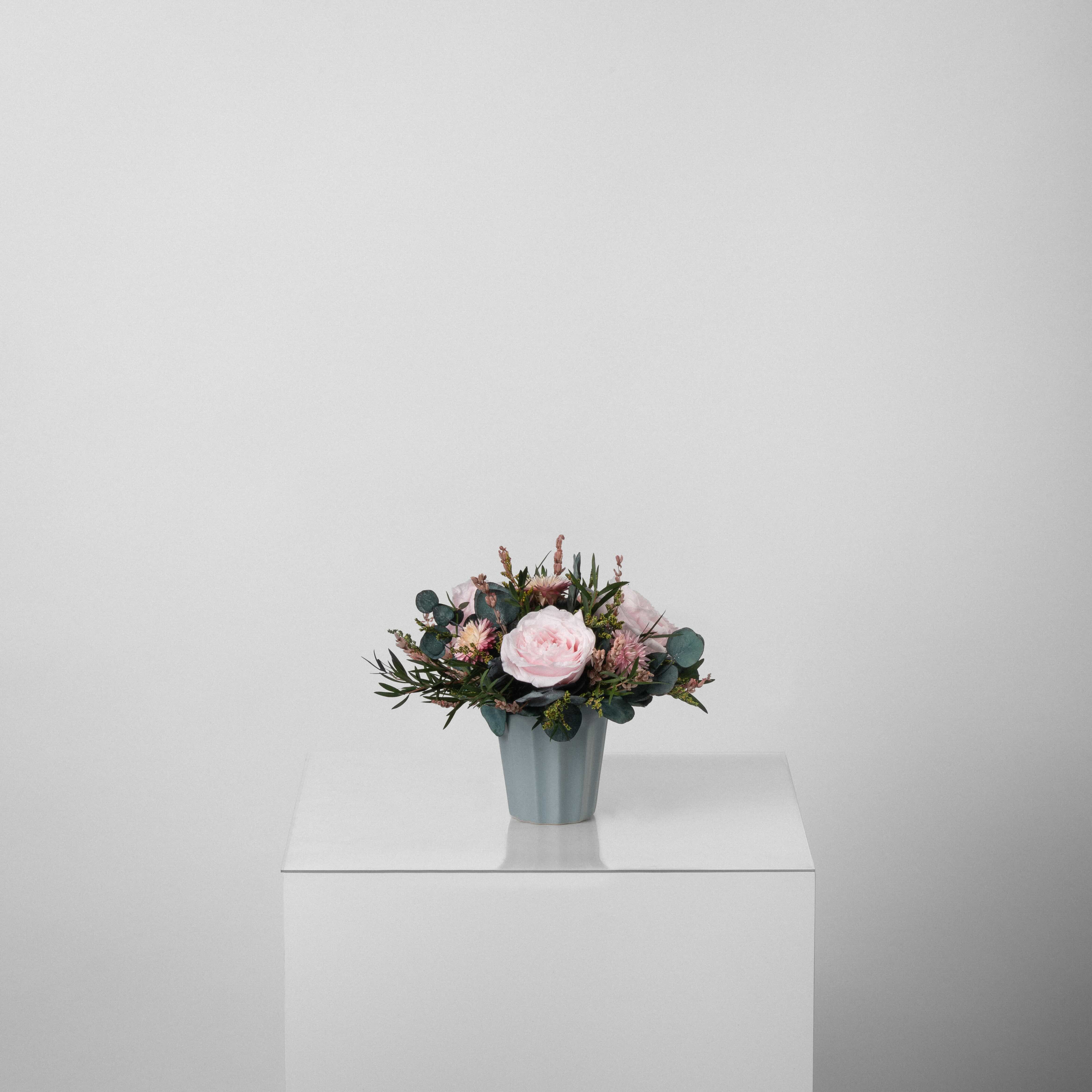 A preserved rose arrangement with preserved foliage in blue vase
