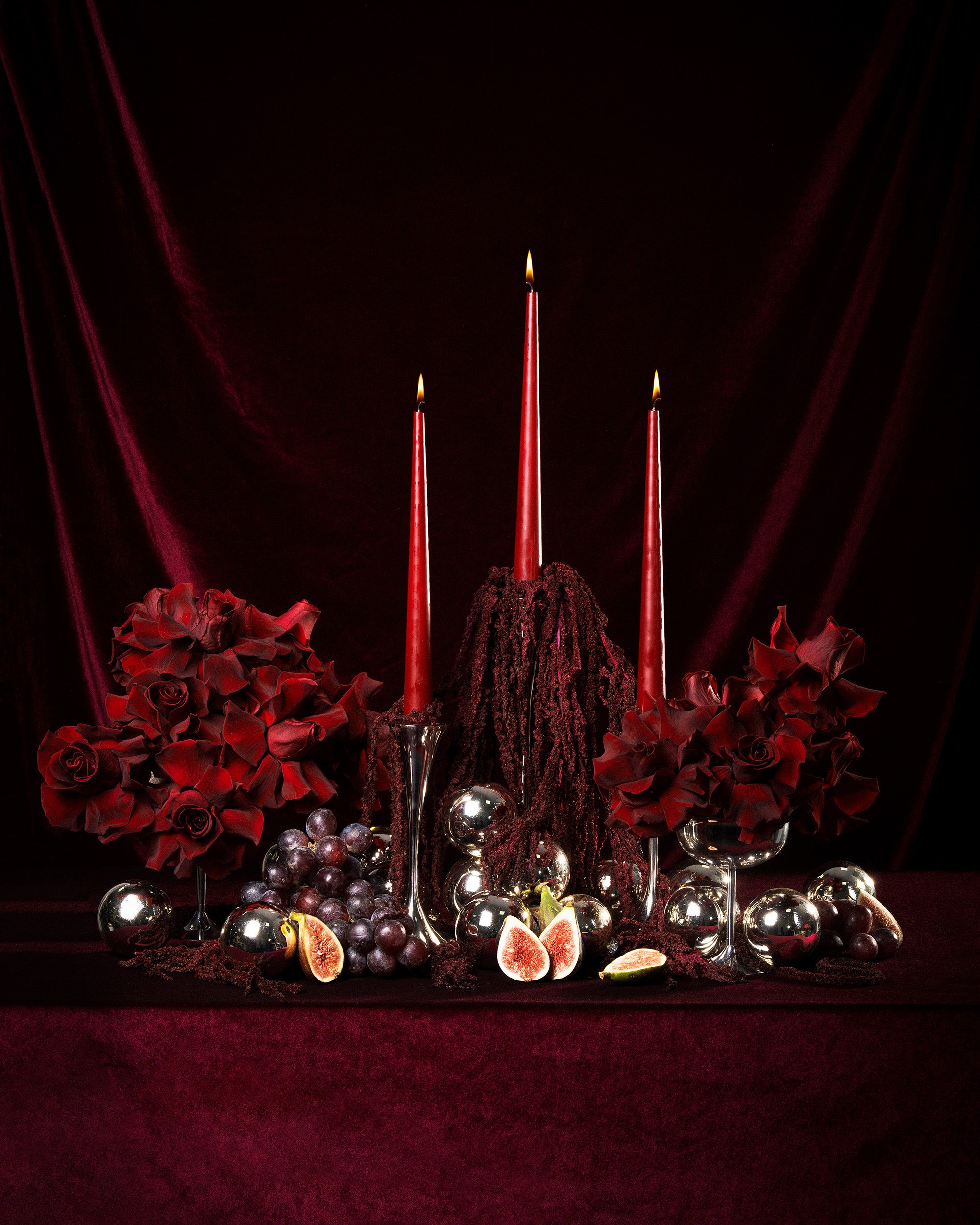 Decorative still life with red candles, preserved roses and amaranthus, and fruits on a dark background