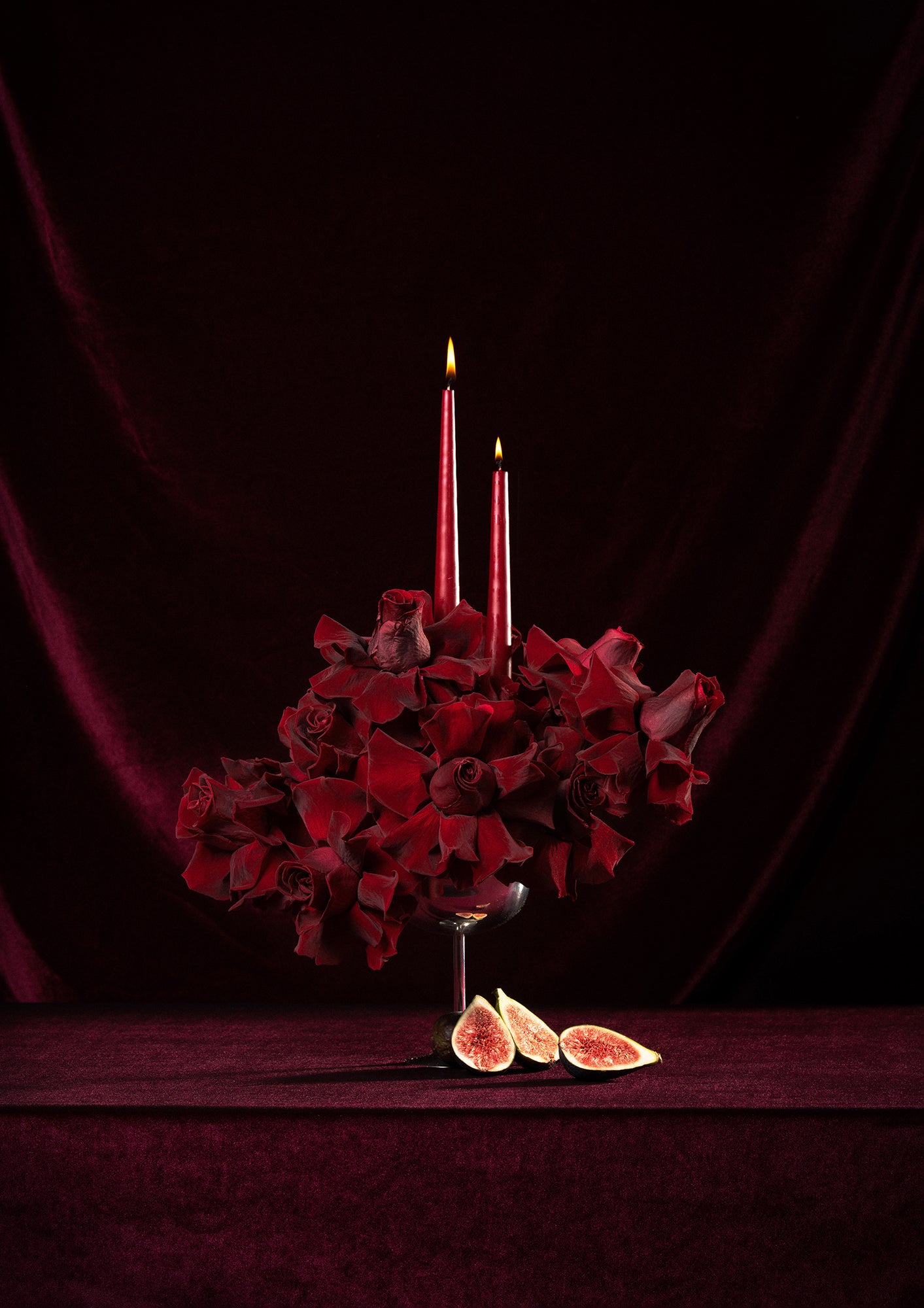 Decorative preserved roses arrangement with red reflexed roses, candles, and figs on a dark background