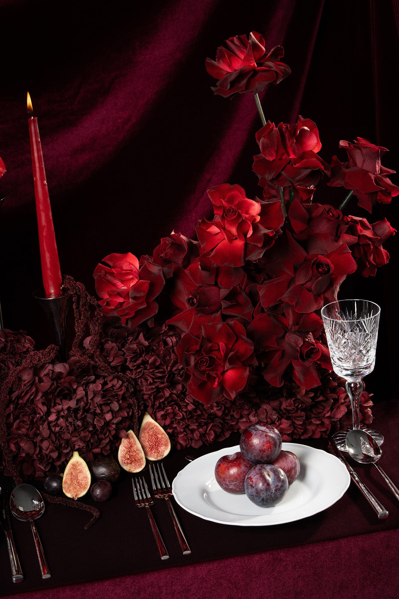 Decorative table setting with red preserved roses and hydrangeas, candles, and fruit on a dark background