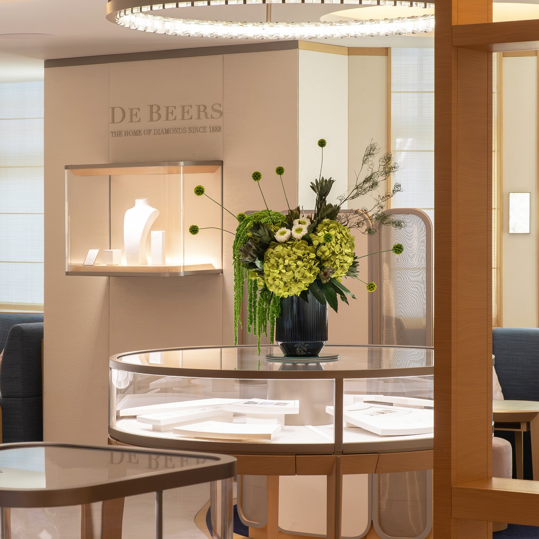 Preserved modern floral arrangement, featuring preserved green hydrangeas, leucadendron, amaranth and scabiosa on a glass table, in De Beers showroom