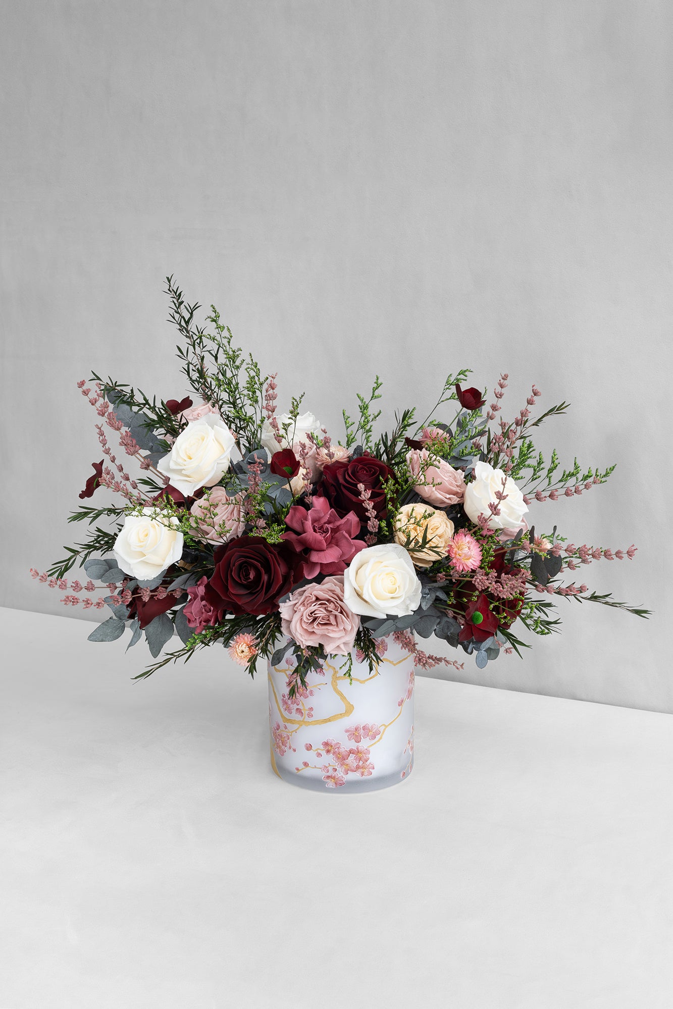 Bouquet of preserved roses, gardenias and poppies with lavender and preserved eucalyptus in a decorative vase on a light grey background