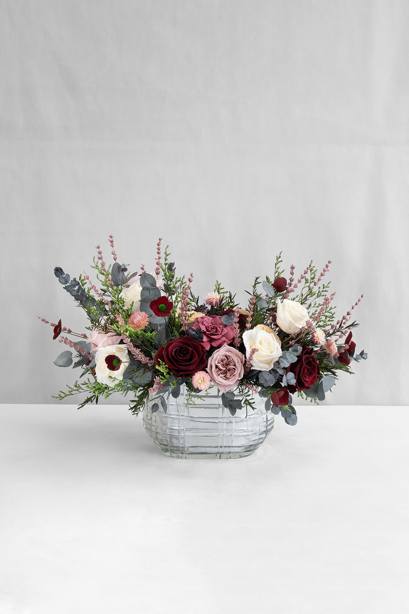 Bouquet of preserved roses, gardenias and poppies with lavender and preserved eucalyptus in a decorative vase on a light grey background