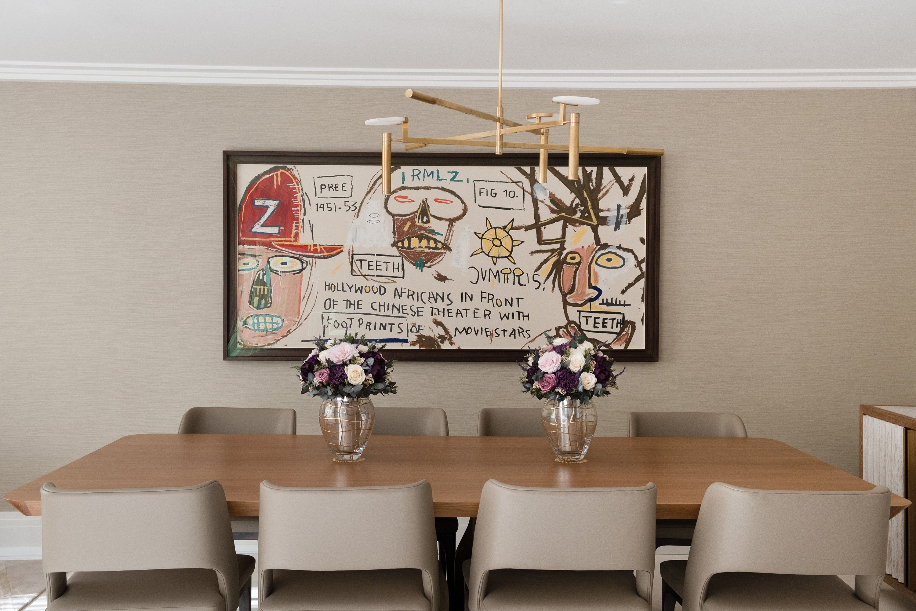Dining room with a large abstract painting on the wall and preserved flower arrangements on the wooden table.