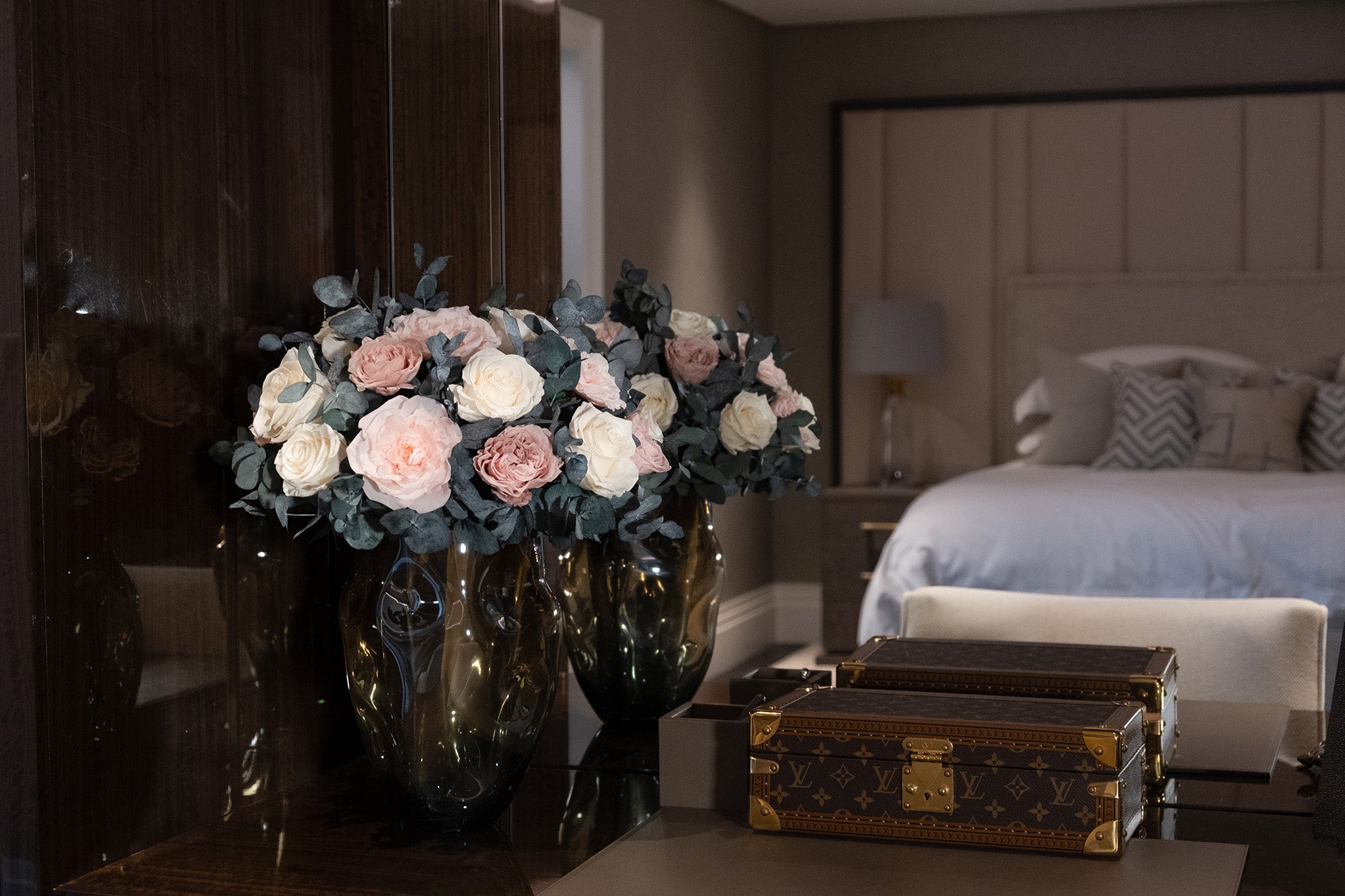 Preserved roses arranged in a vases on a table with a bedroom in the background