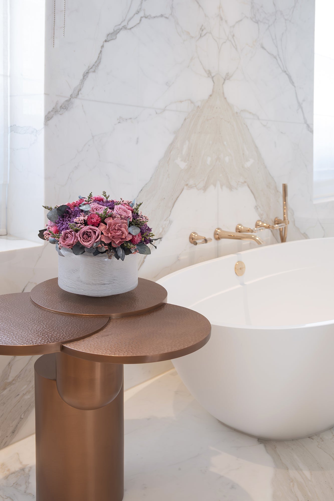 Decorative table with a preserved roses and gardenias arrangement next to a bathtub in a bathroom setting.