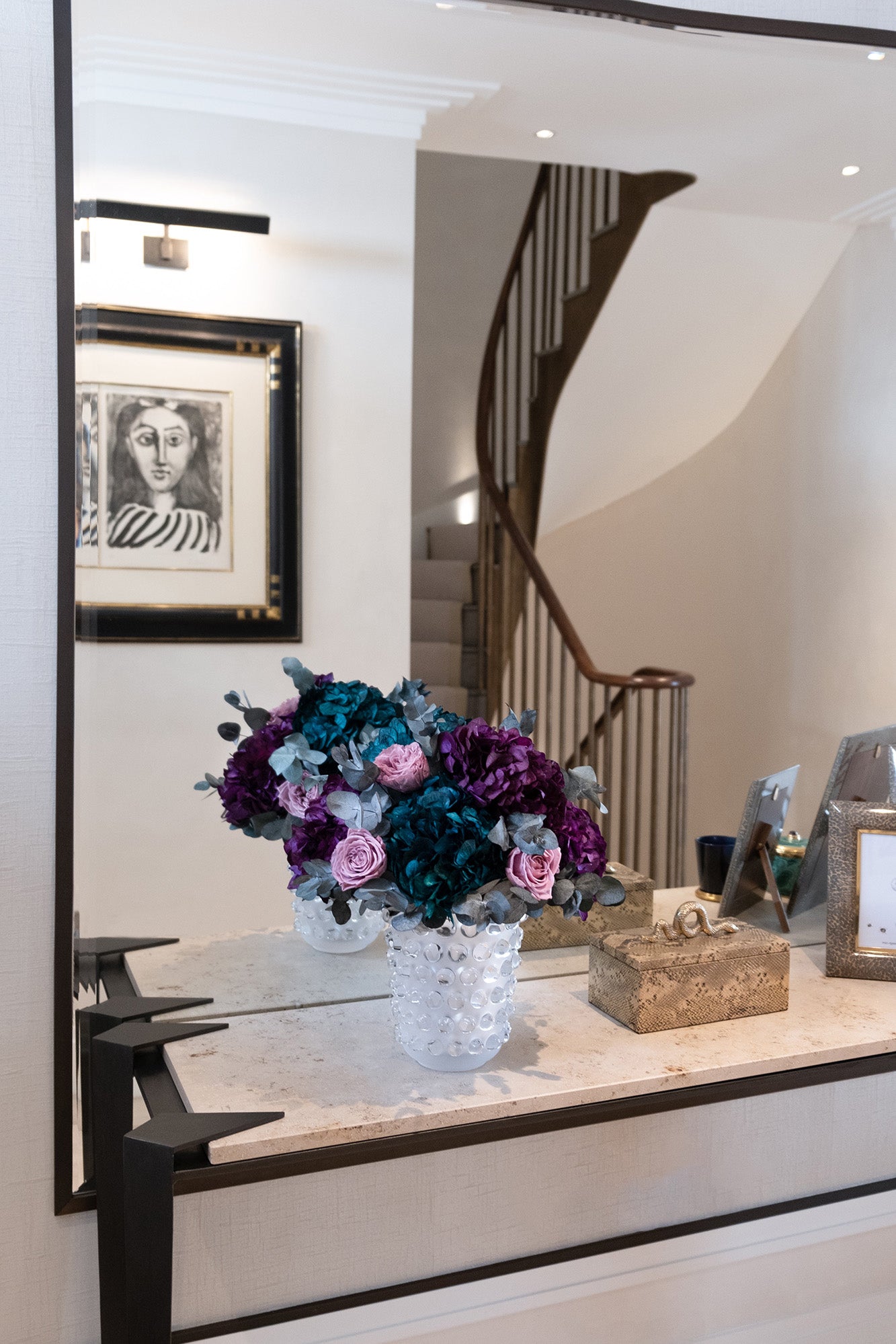 Decorative vase with preserved flowers on a table in a room with framed artwork.