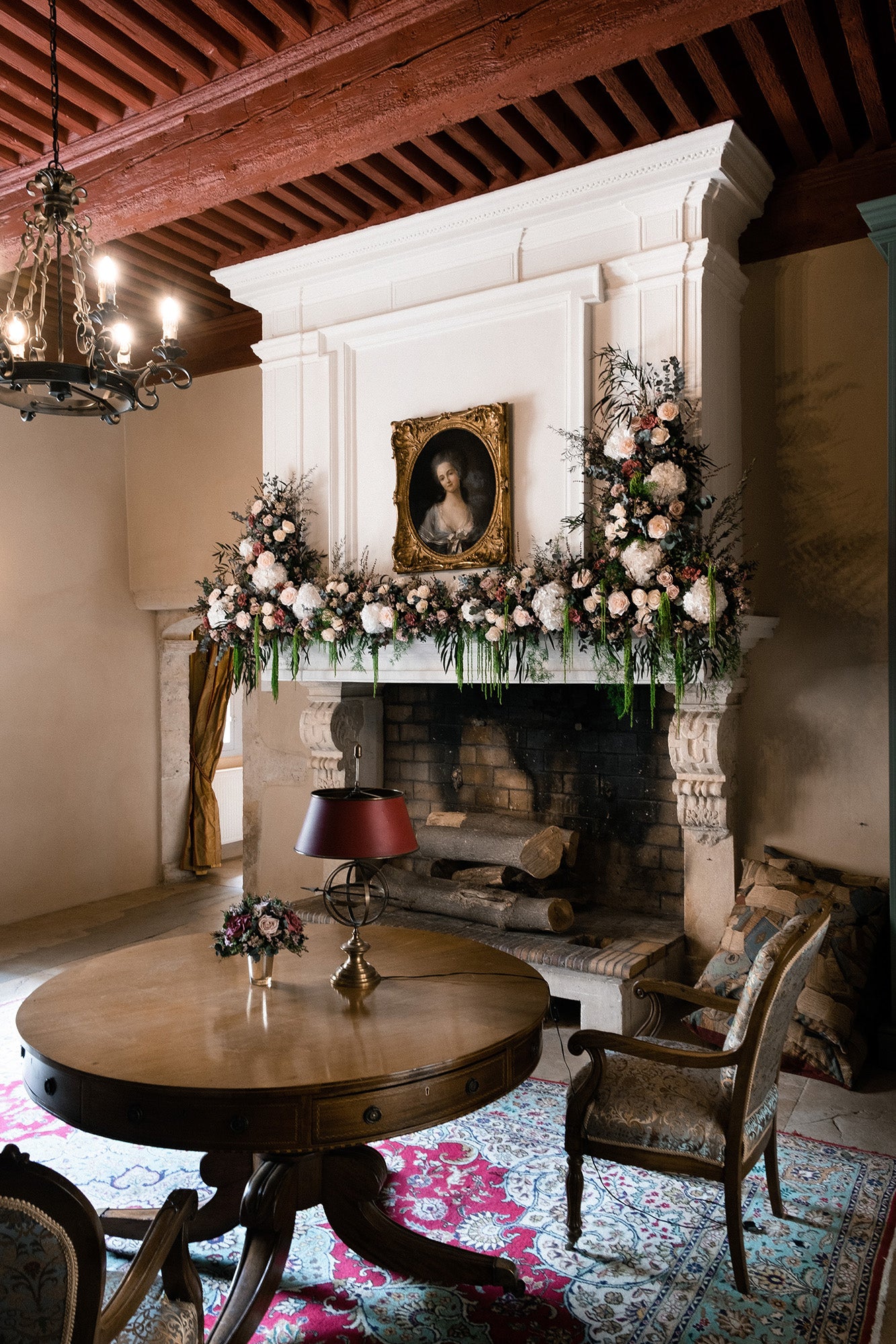 Decorative room with preserved floral arrangement and preserved floral mantle piece, a fireplace, and a wooden table.