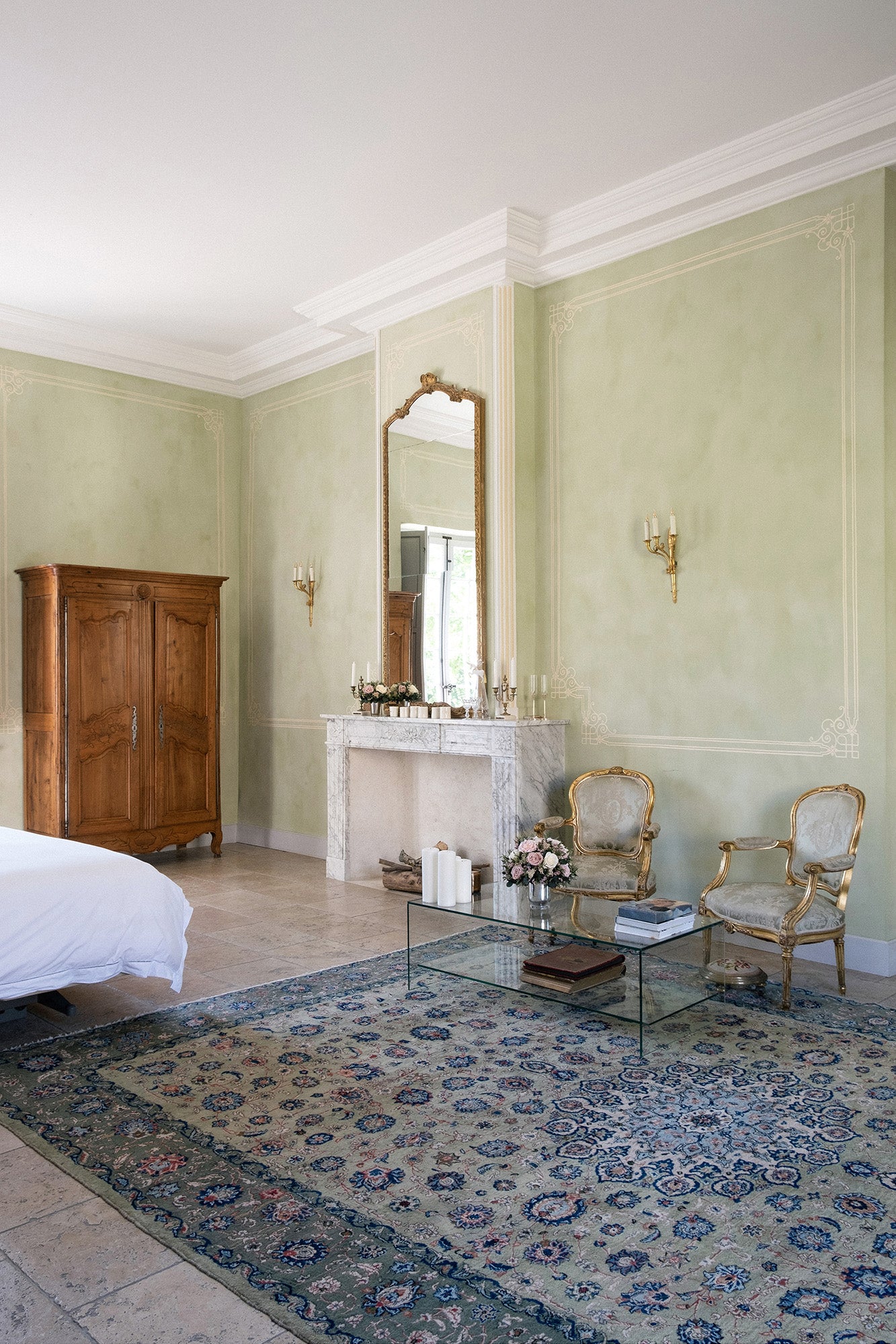 Luxurious bedroom with green walls, two preserved mixed flower arrangements, and decorative rug.