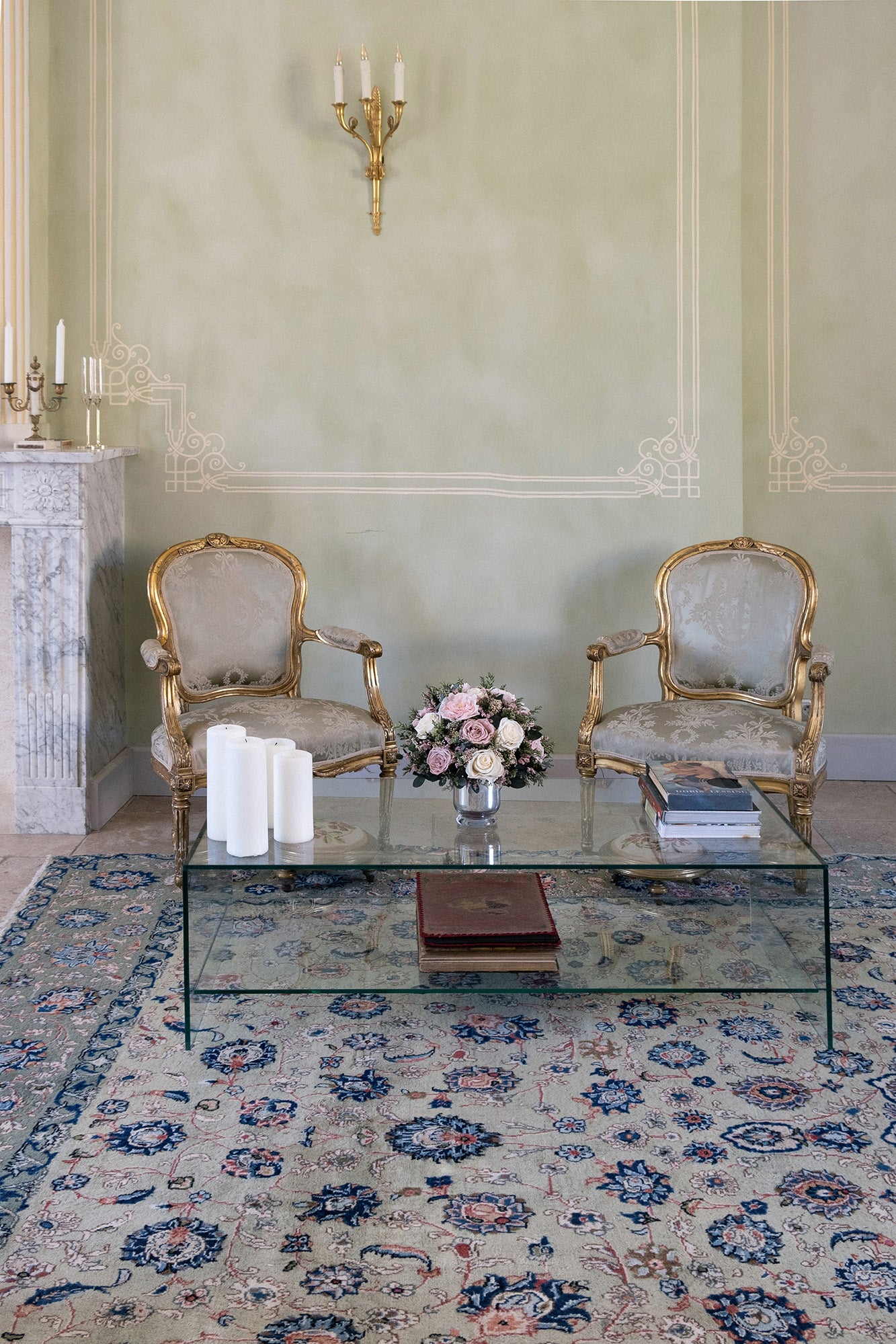 Living room with ornate chairs, glass coffee table, and preserved mixed flower arrangement on a patterned rug.