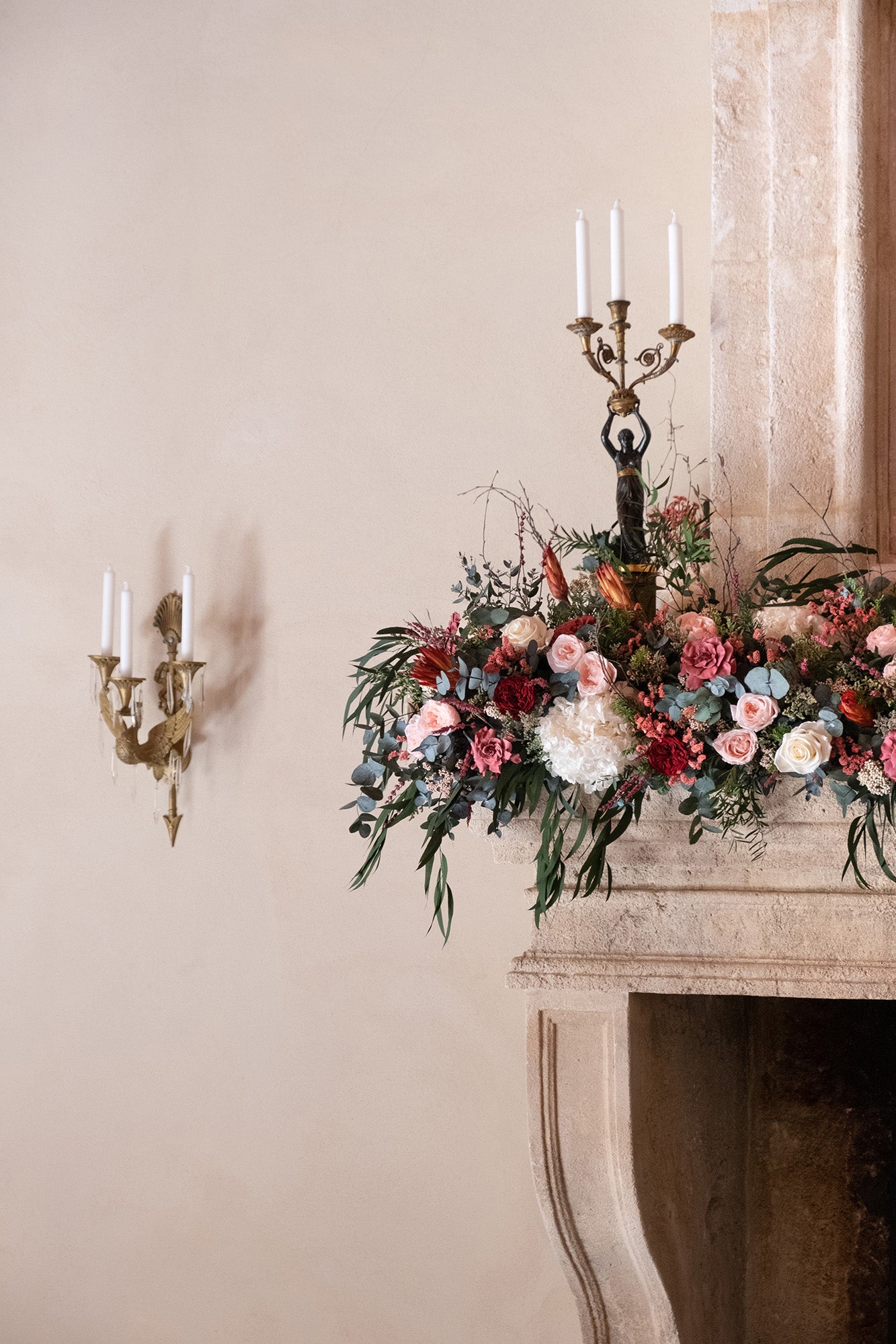 Preserved mixed floral arrangement on a fireplace mantel with a candle holder