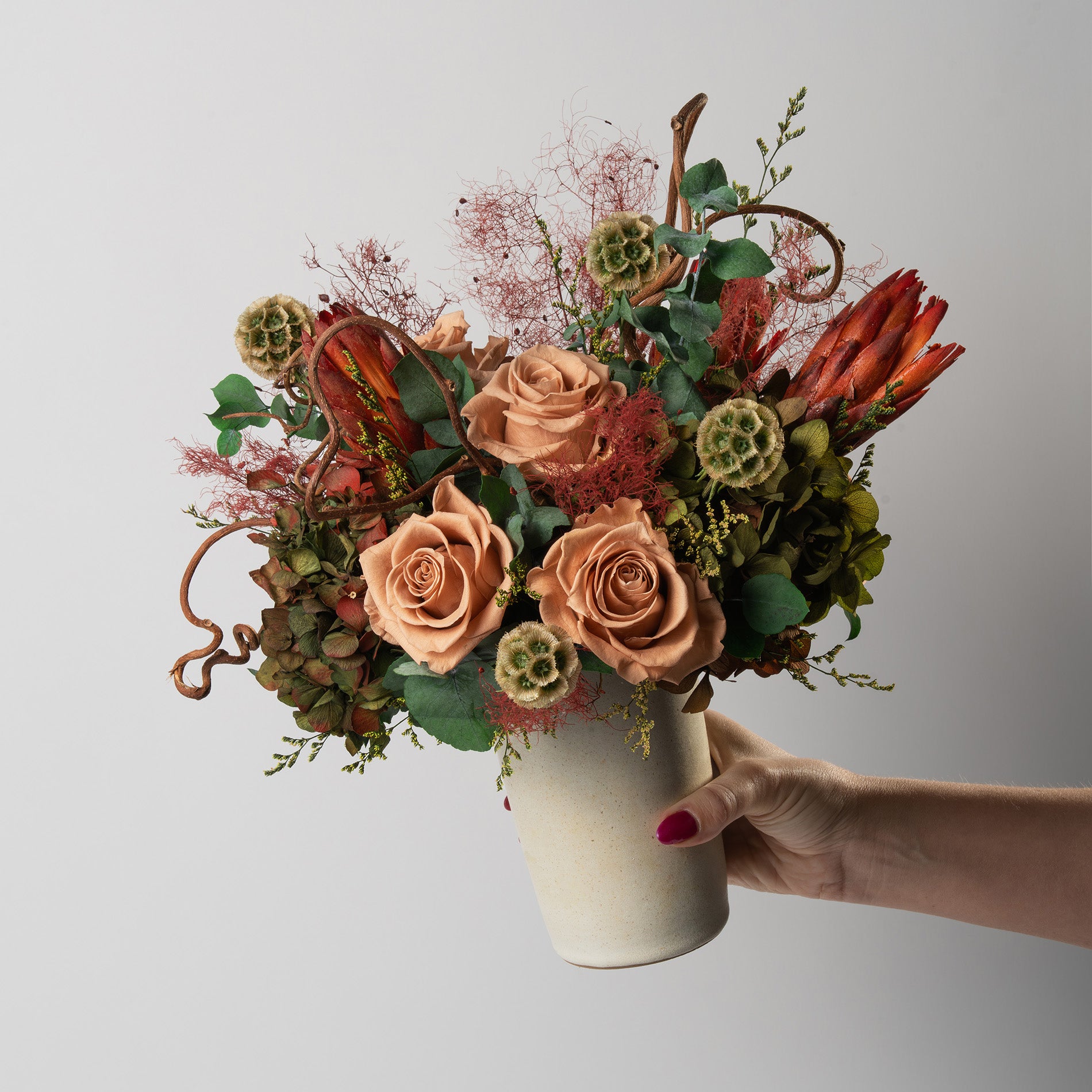 Bouquet of toffee and green mix preserved flowers in a ceramic vase on a white background