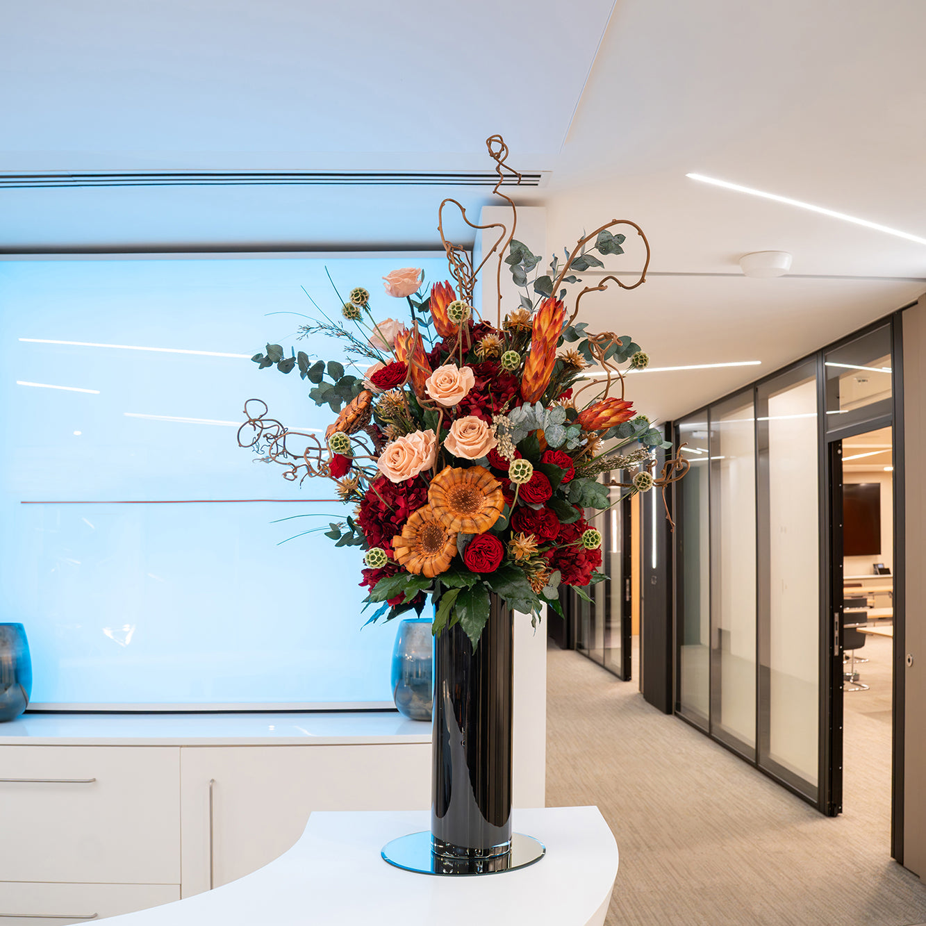 Preserved mixed flower arrangement in a tall black vase displayed in a modern office