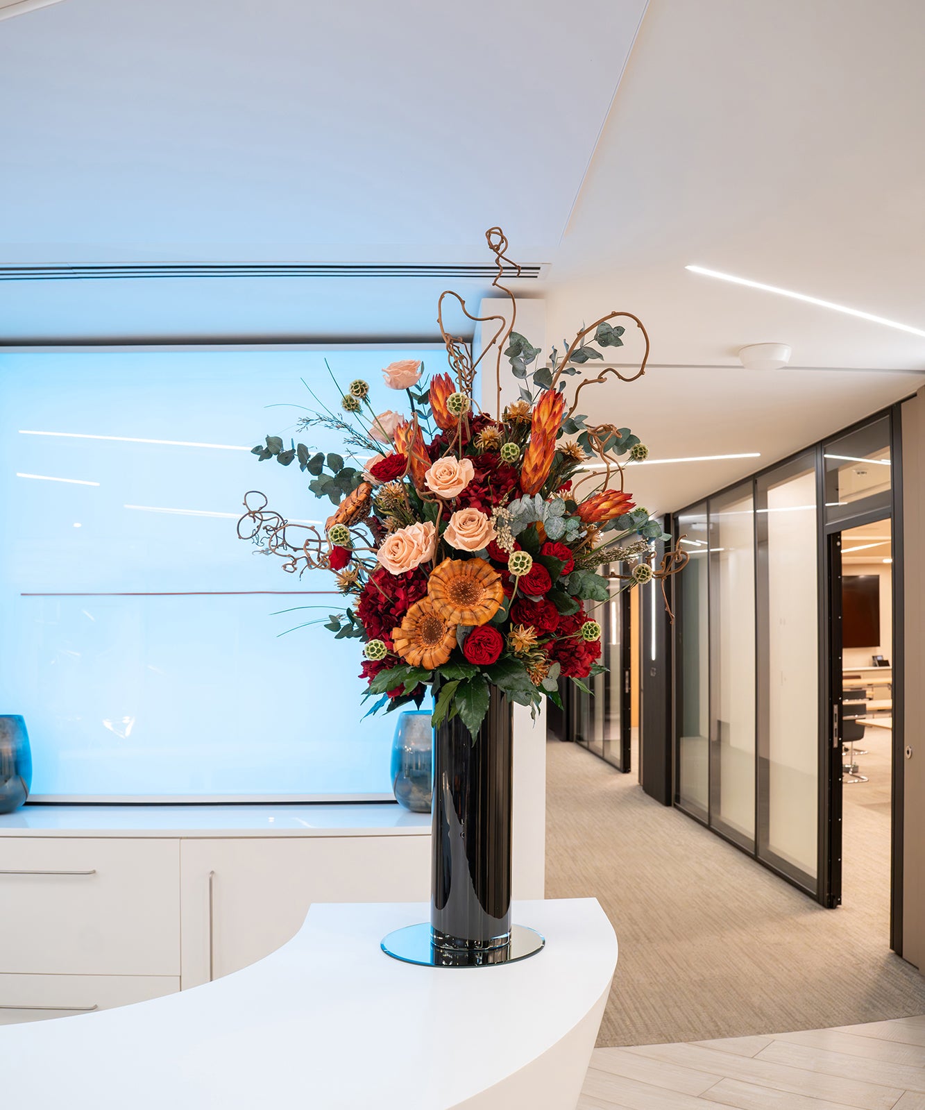 Preserved mixed flower arrangement in a tall black vase displayed in a modern office