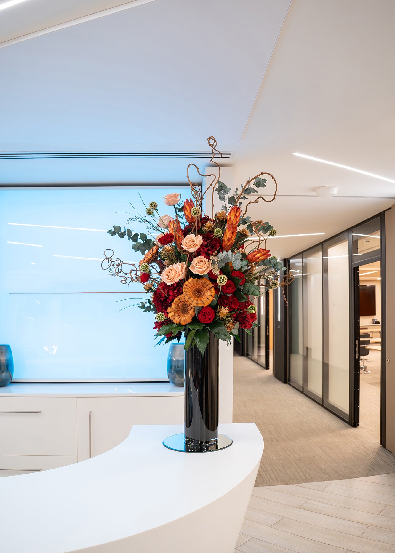 Preserved mixed flower arrangement in a tall black vase displayed in a modern office