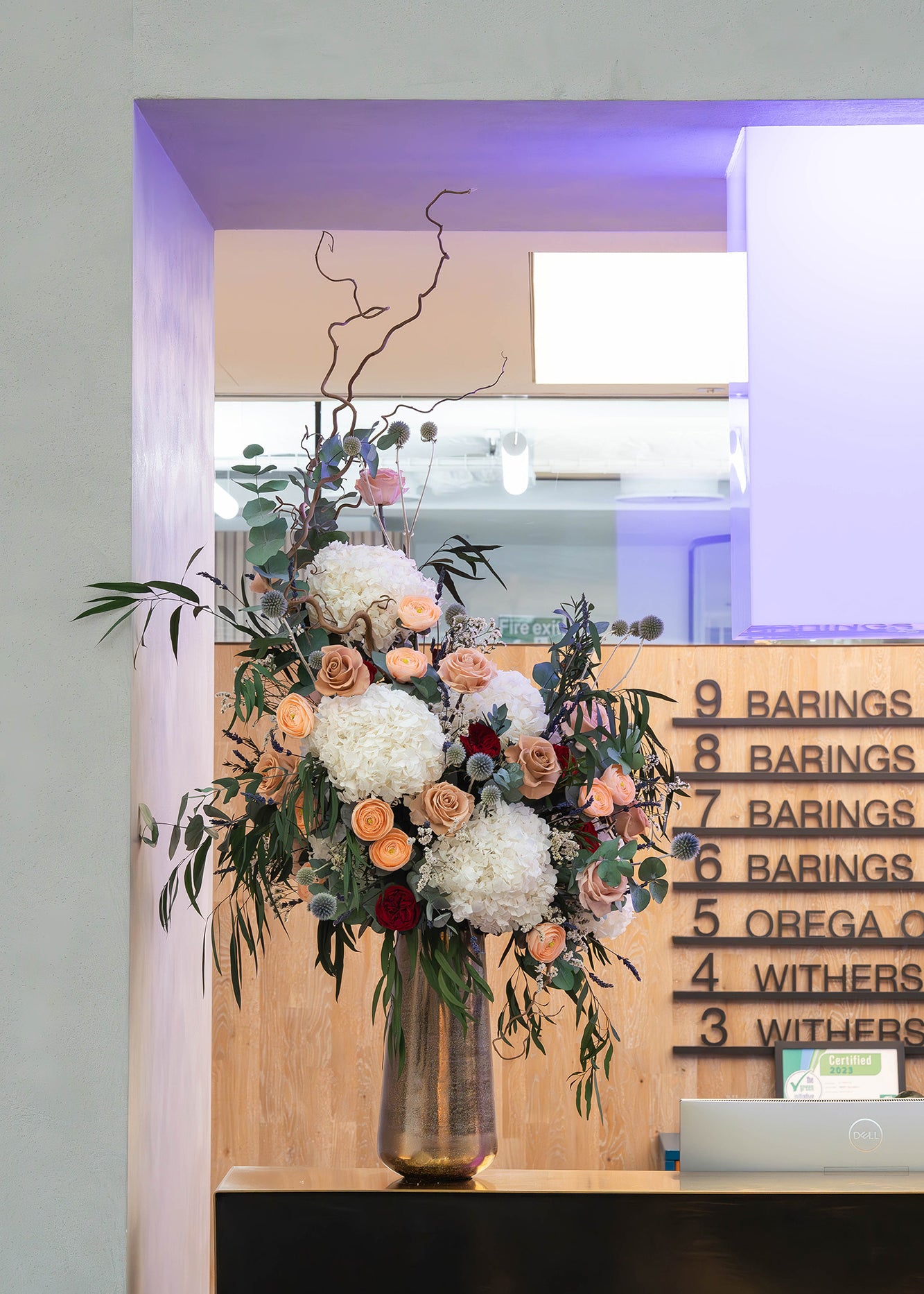 Preserved flower arrangement in a gold vase displayed in a modern office lobby